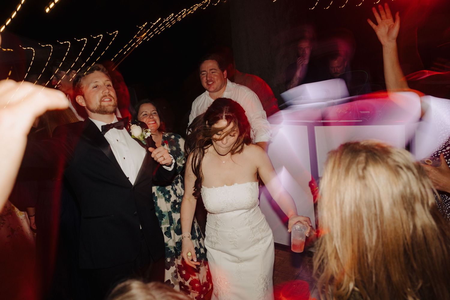 Wedding reception dance floor filled with guests celebrating under dim lighting.