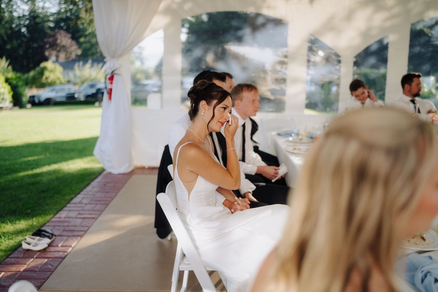 Wedding guests seated under a white tent canopy during an outdoor ceremony.
