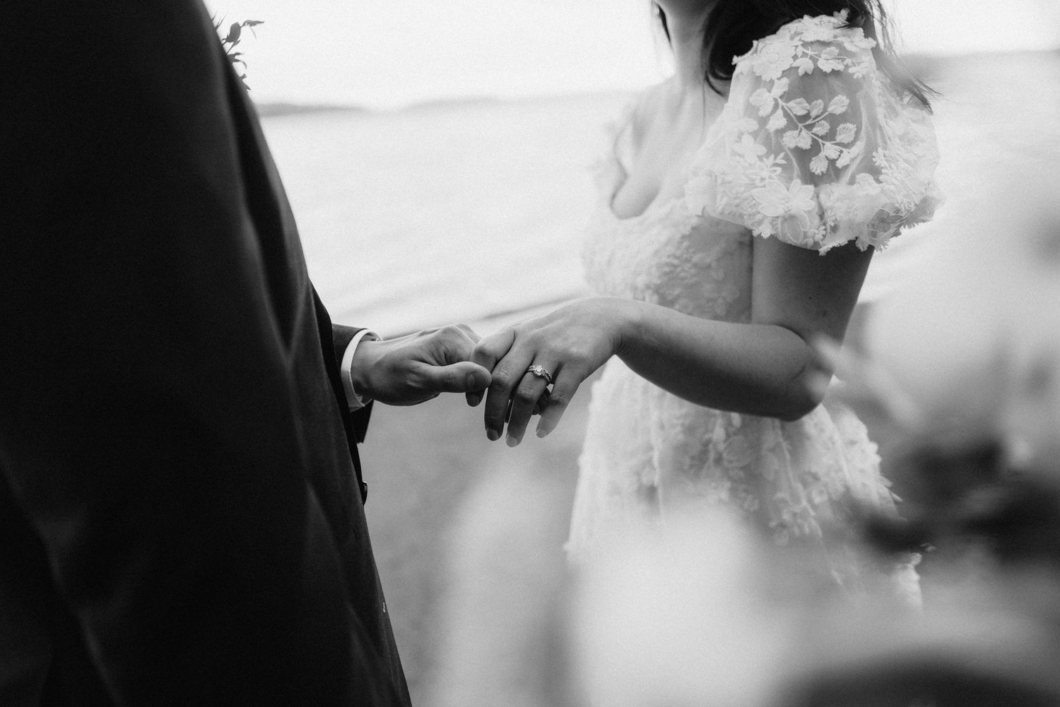 Black and white close up photo of hands exchanging rings during a wedding ceremony.