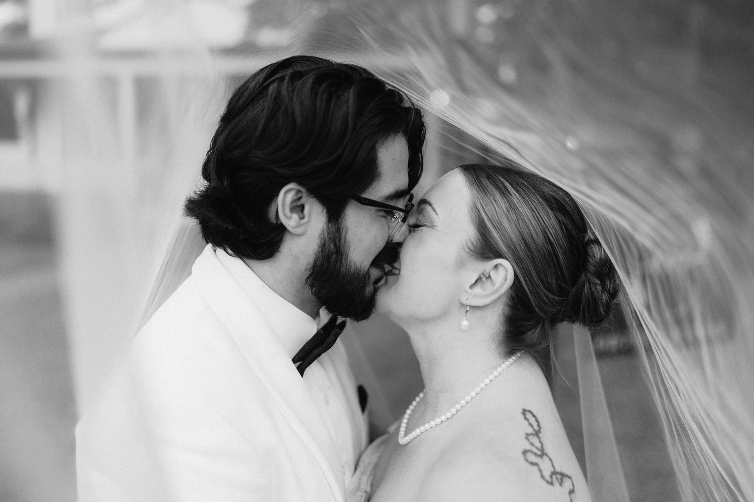 A romantic black and white portrait of newlyweds sharing an intimate moment under a veil.