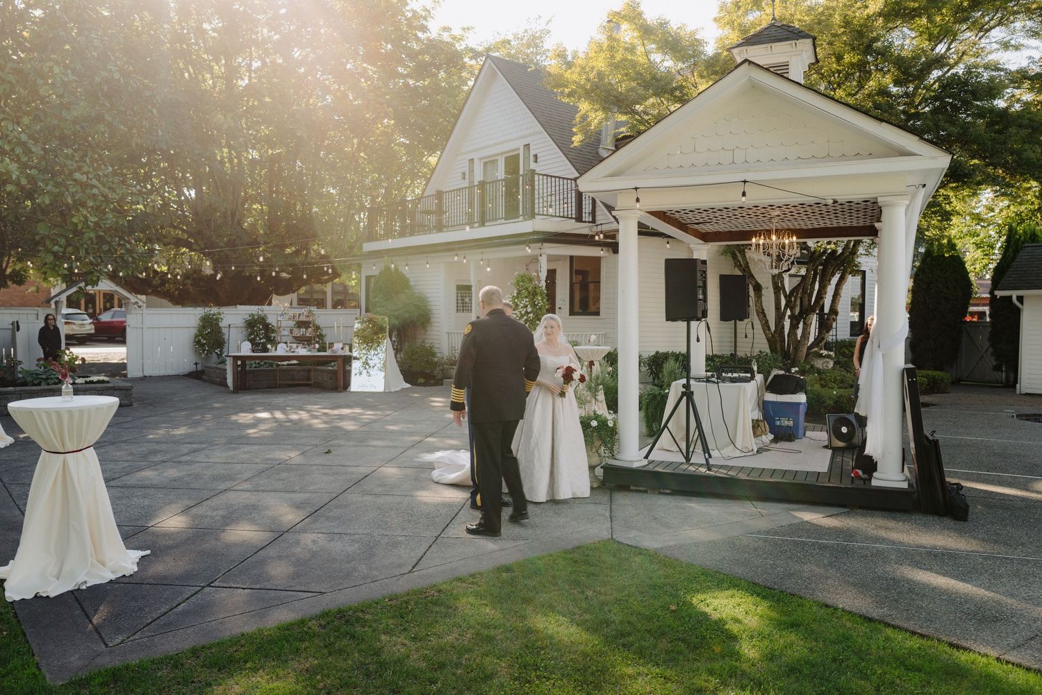 Panoramic view of a white house exterior with trees and sunlight during a wedding setup.