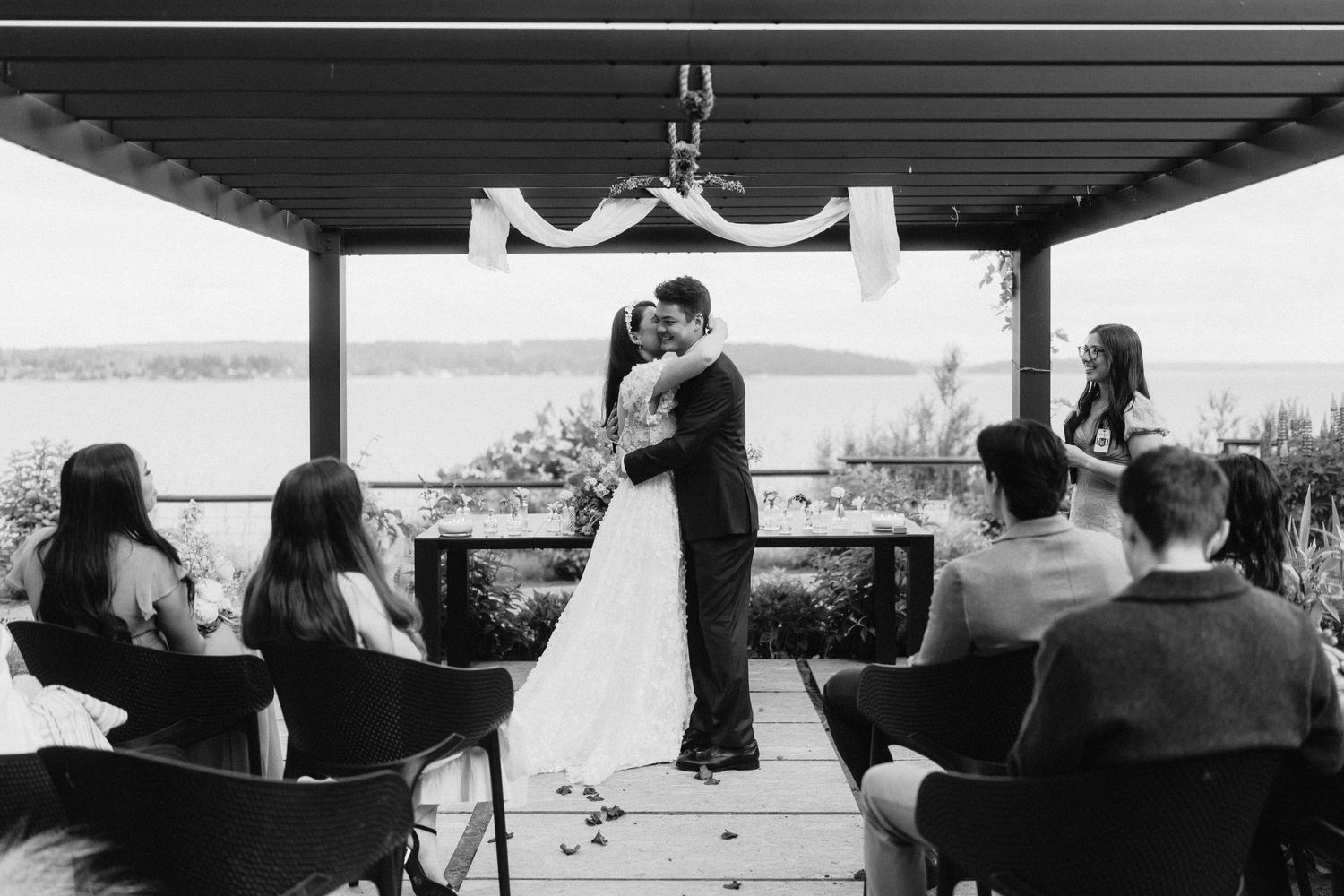 A waterfront wedding venue with black chairs and decorative elements under a covered patio.