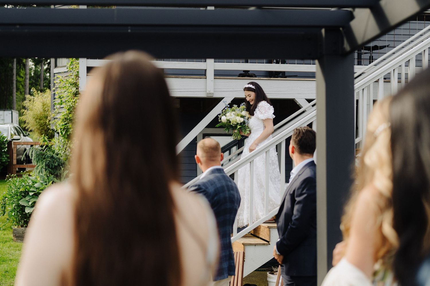 Wedding ceremony guests seated outdoors under a covered pavilion structure.