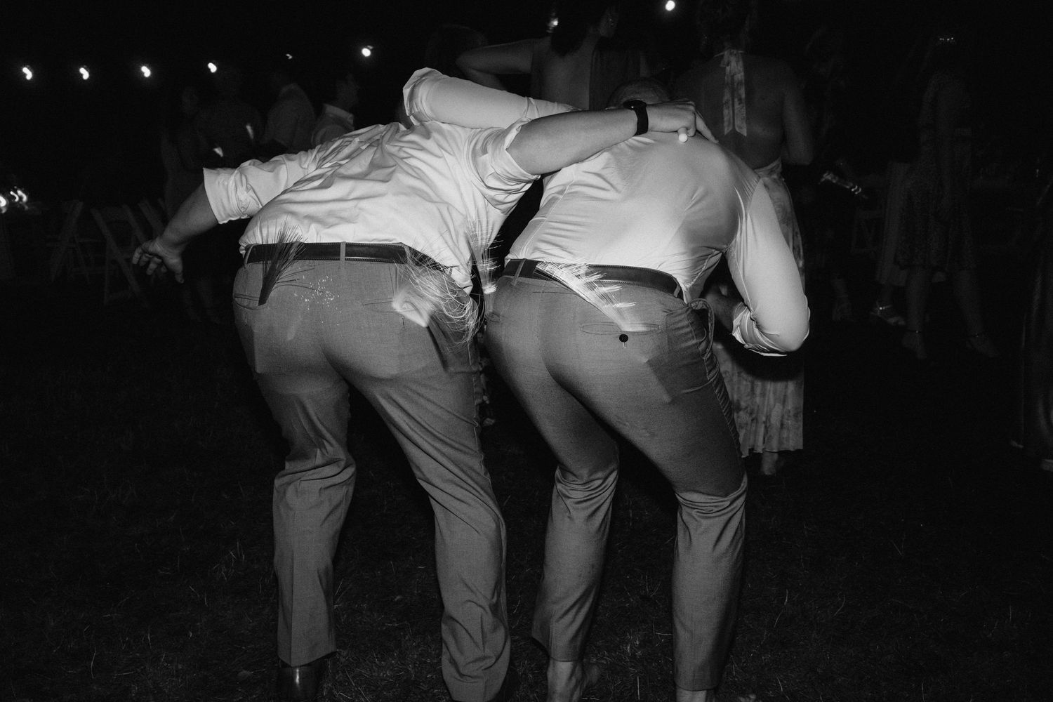 Black and white photo of groomsmen bending over in matching suits on dance floor.