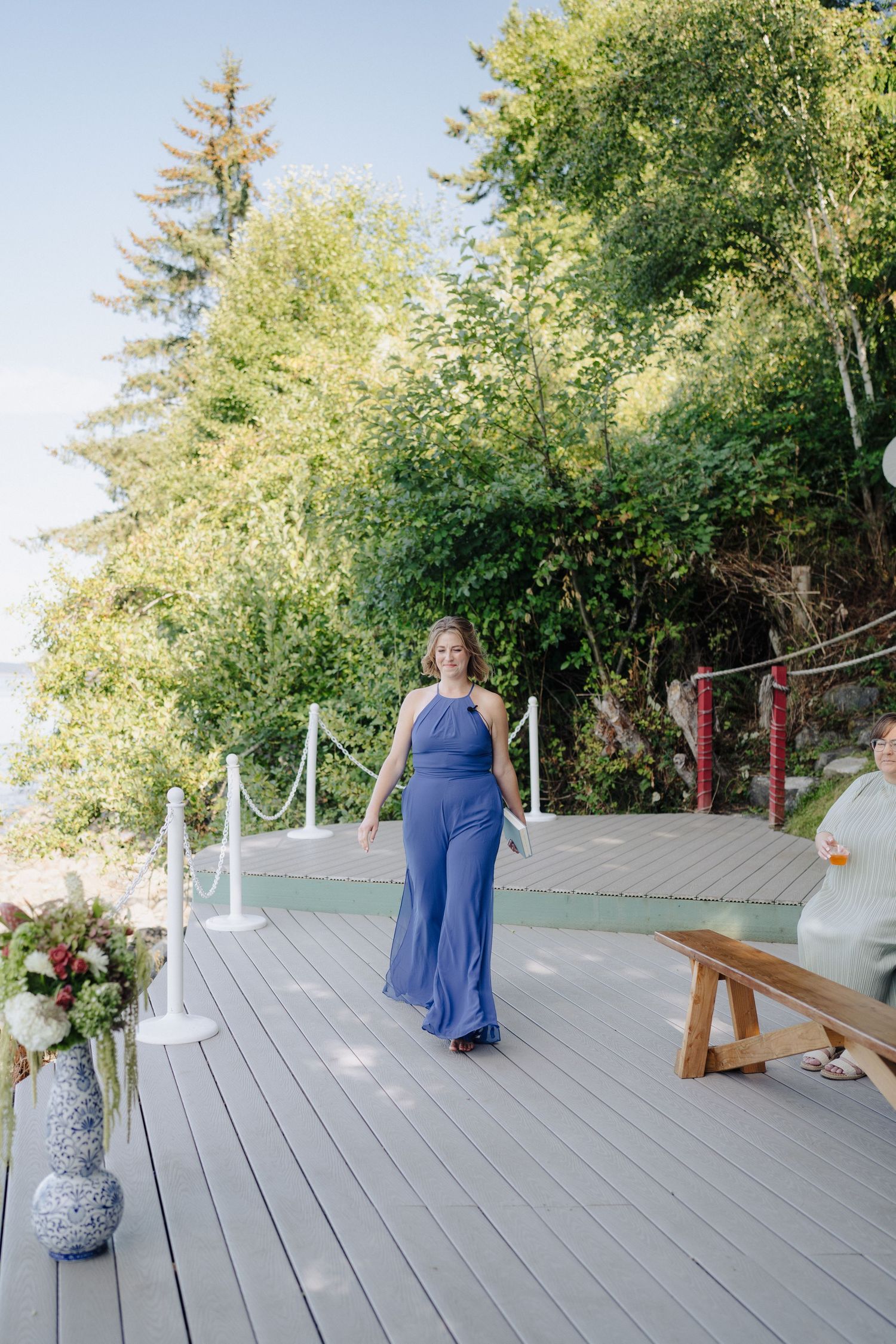 An outdoor deck surrounded by trees features wooden benches and white decorative elements.