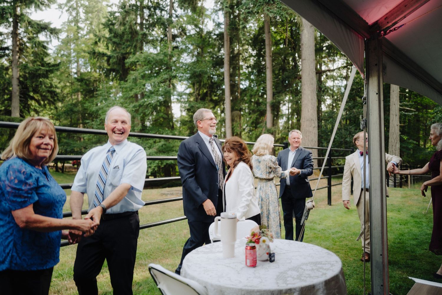 Outdoor wedding reception under white tent with guests mingling and dancing.