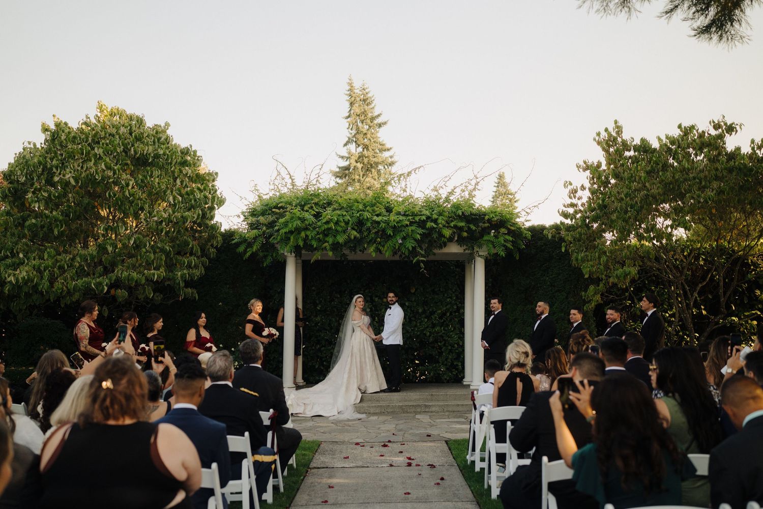 Wedding ceremony setup with white chairs and natural landscaping in late afternoon light.