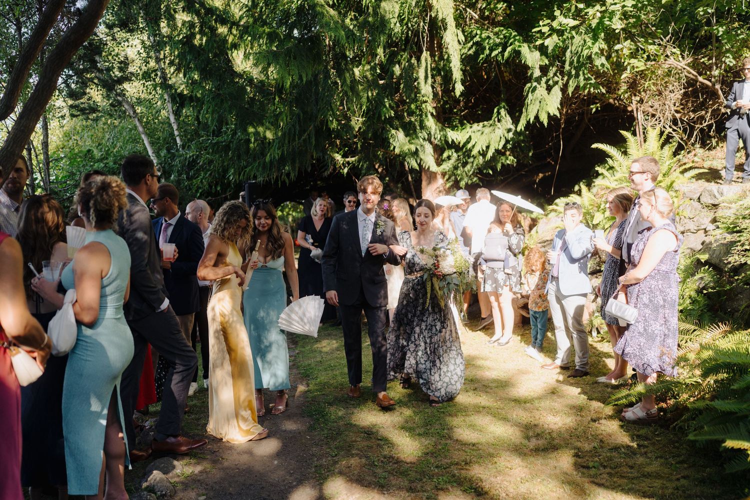 Wedding guests gather in a lush garden setting surrounded by greenery and natural light.