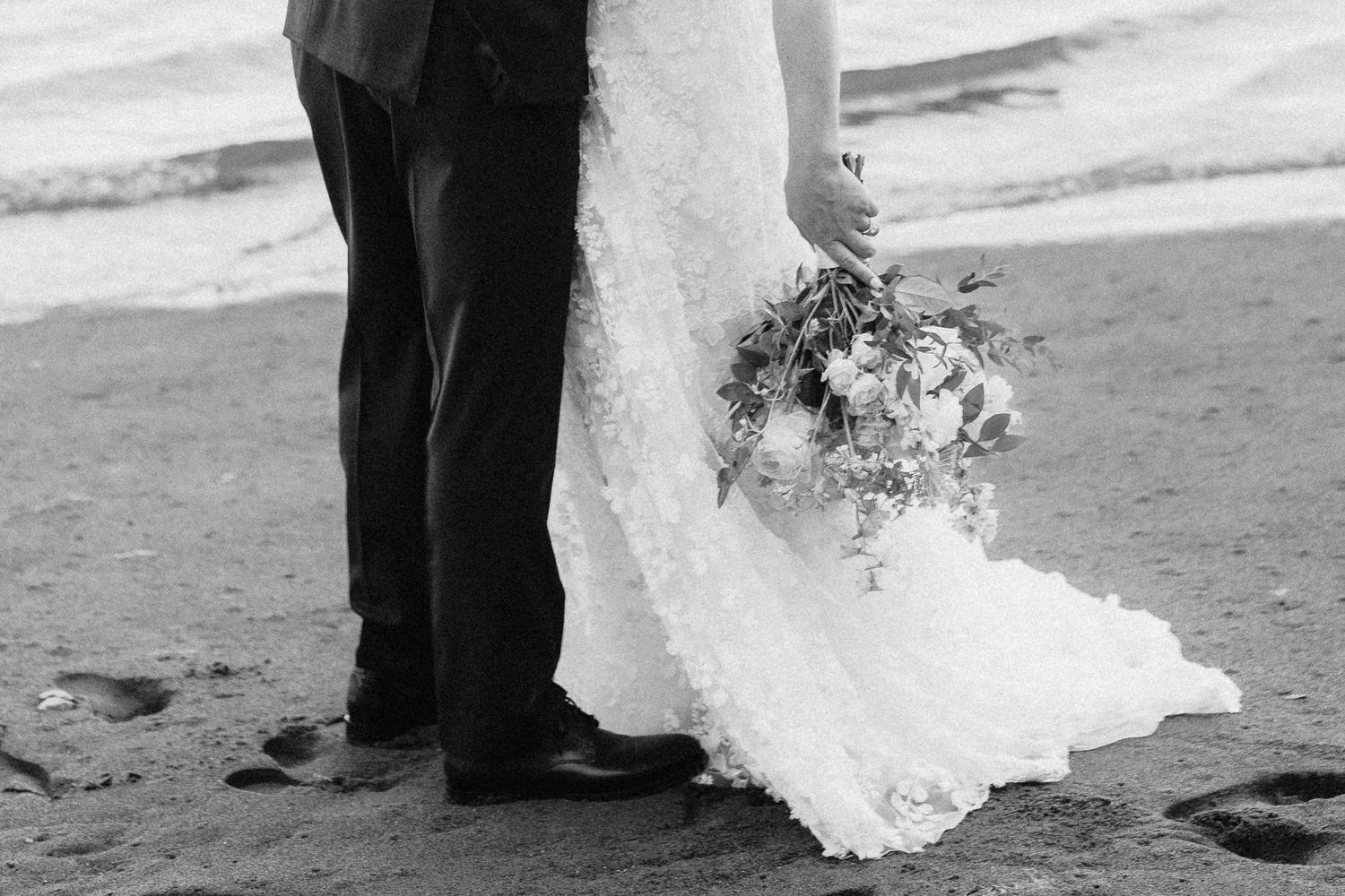 A couple dances together on a beach with the bride's white dress flowing in the breeze.