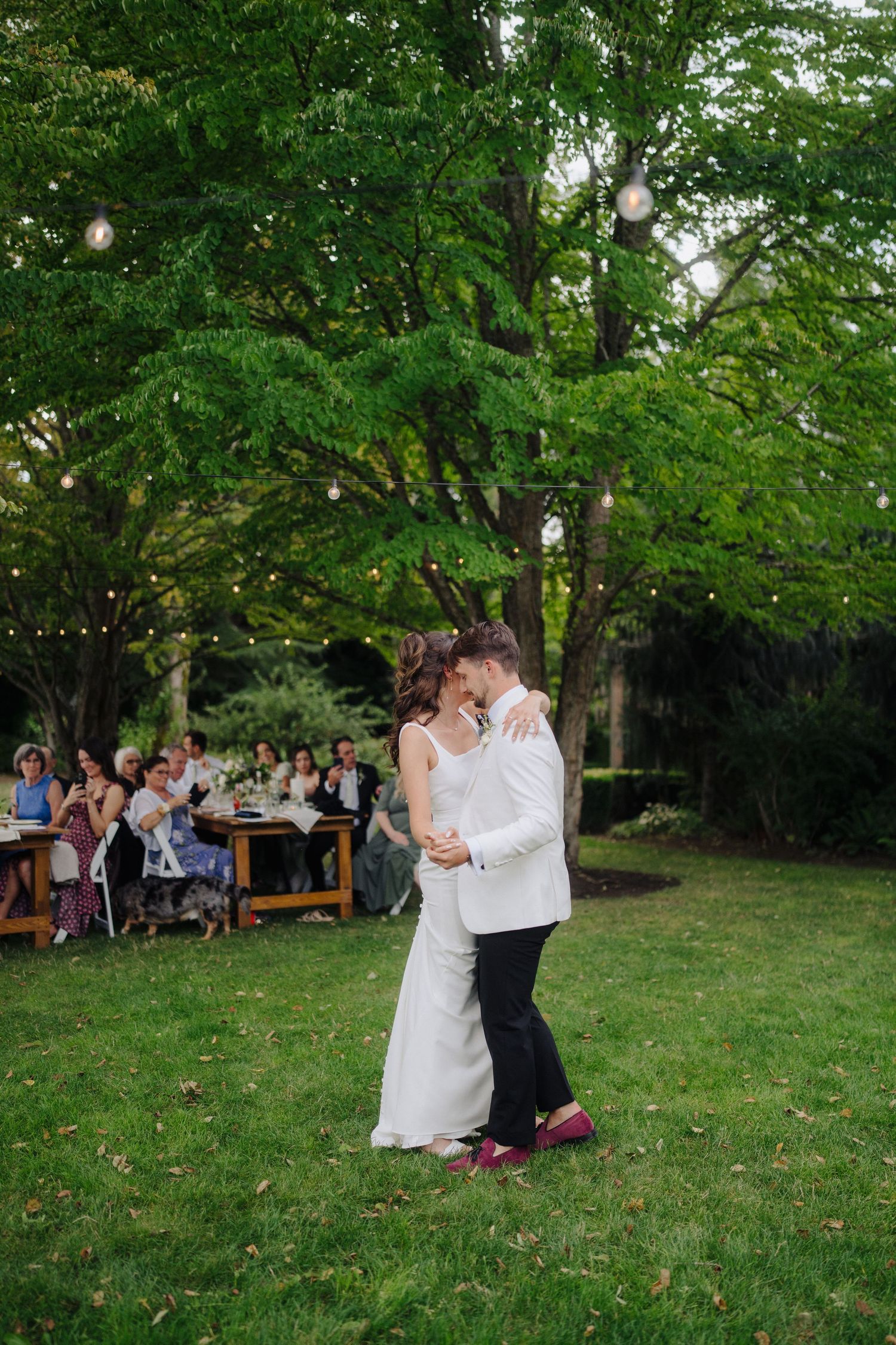 Couple shares an intimate moment on a grassy lawn during outdoor wedding celebration.
