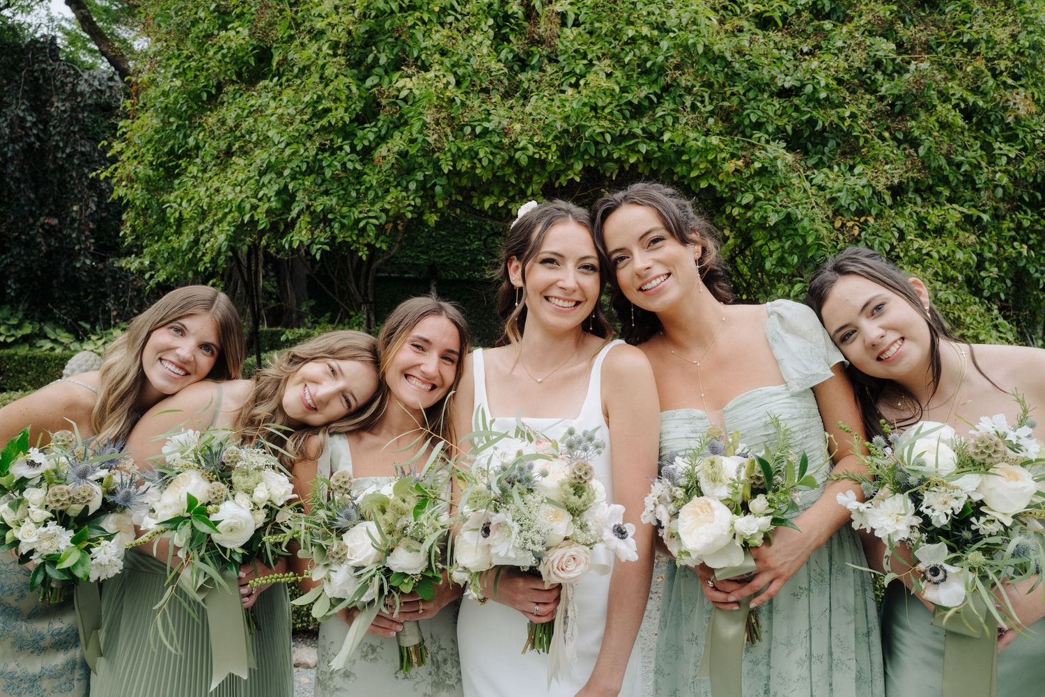 Row of bridesmaids in mint green dresses holding white bouquets smile for a group photo.