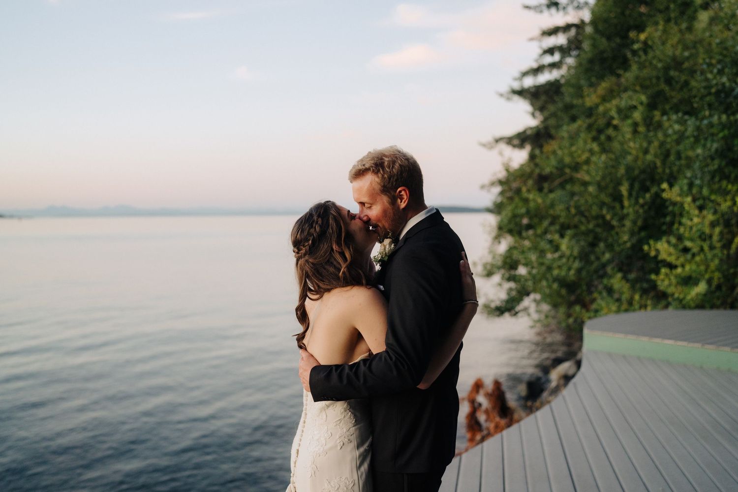 Romantic wedding photos captured on a waterfront deck during golden hour with scenic ocean views.