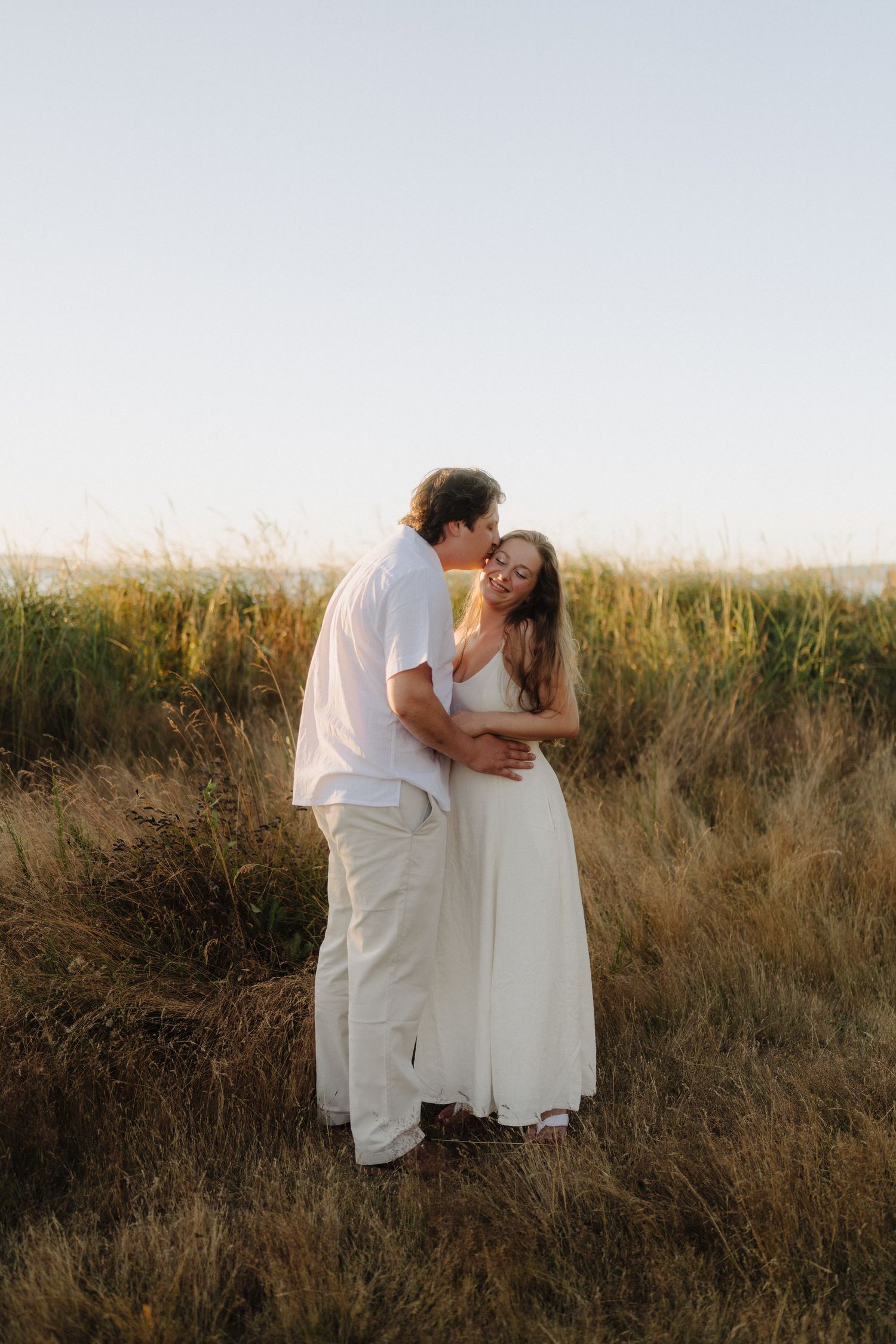 Romantic couple embraces in golden field during sunset photoshoot.