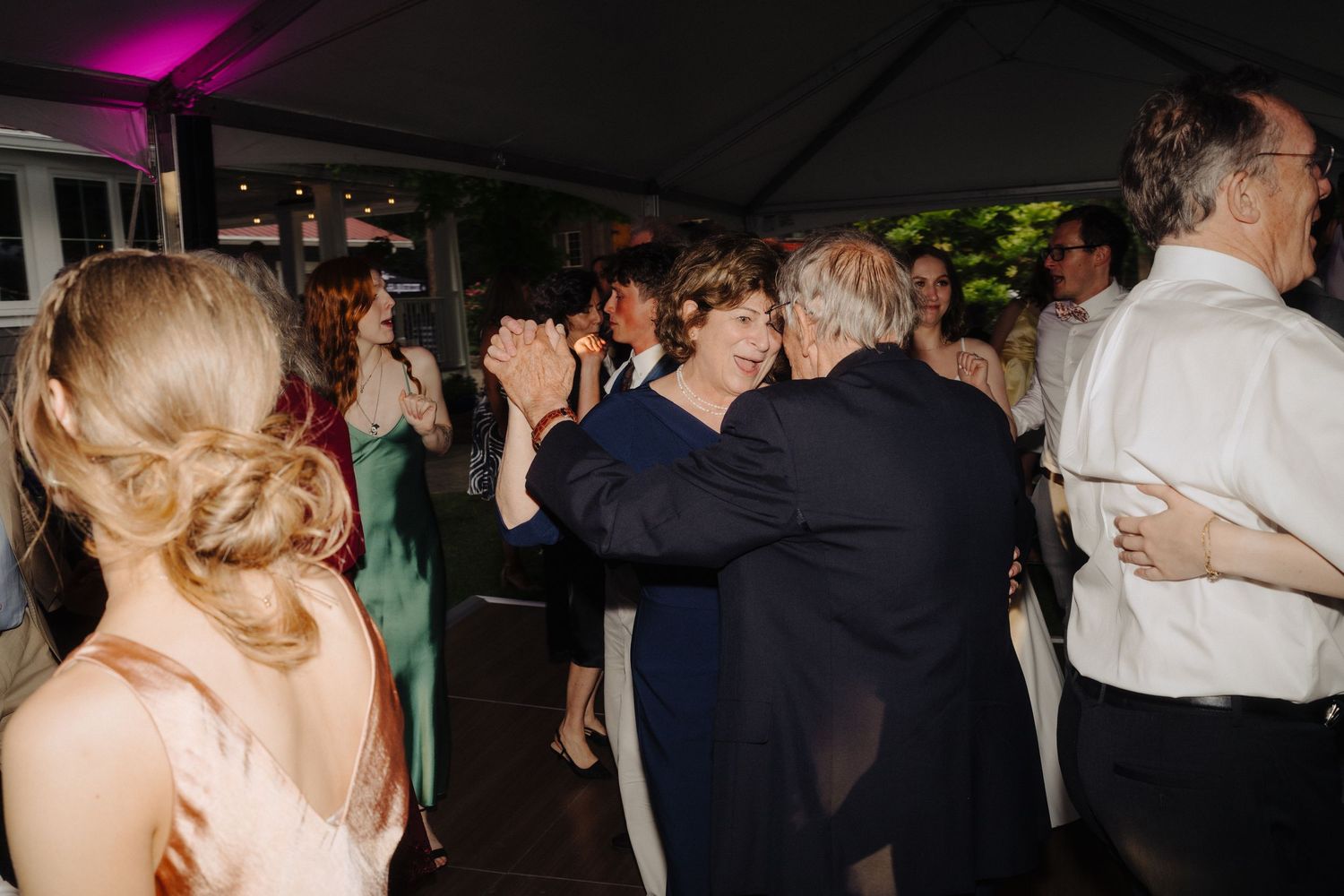Wedding reception dance floor filled with guests under purple mood lighting.