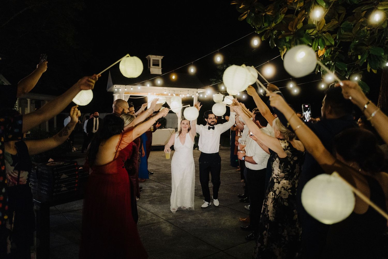 Wedding reception dance floor illuminated by hanging paper lanterns and string lights.