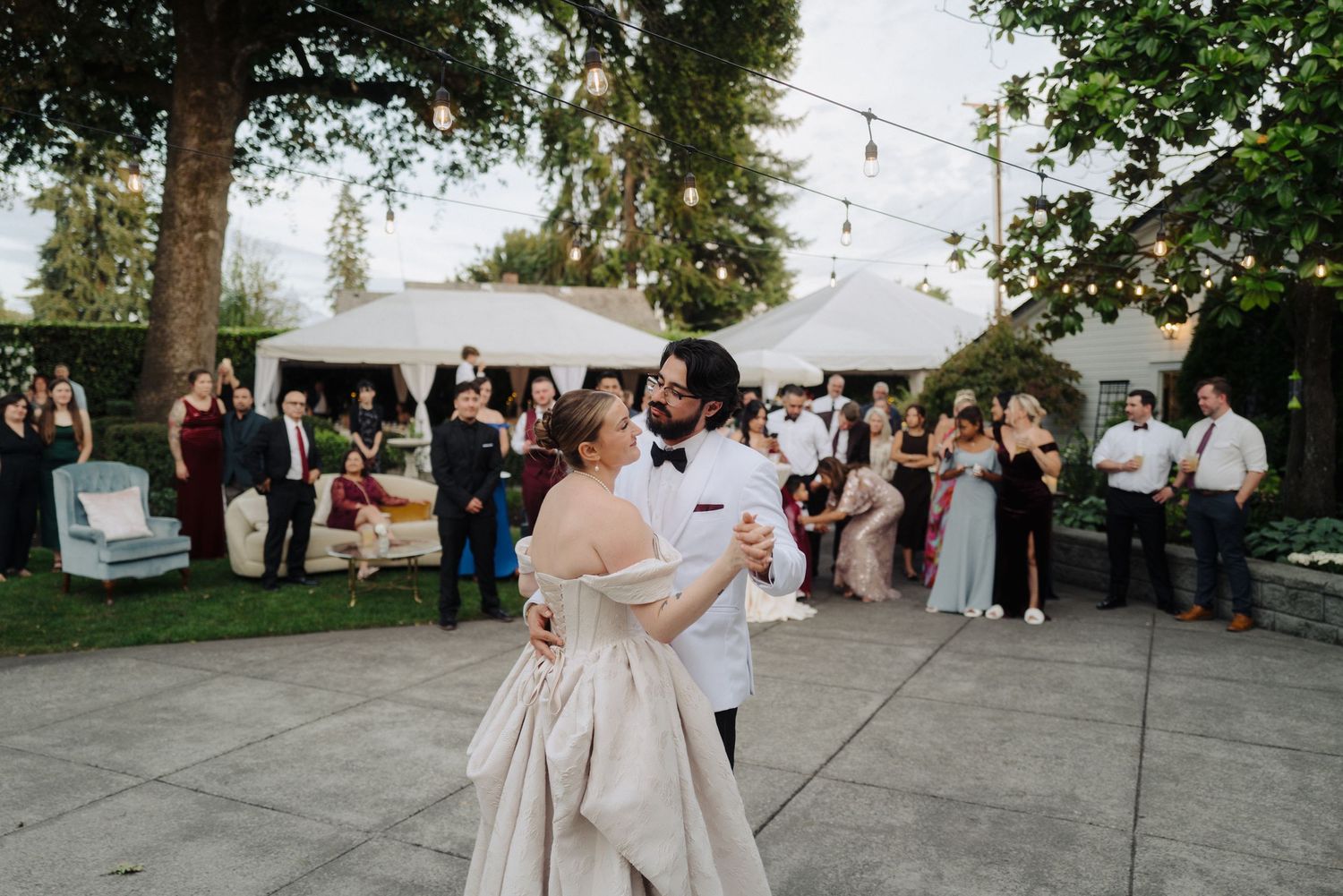 Evening outdoor wedding reception with guests mingling under string lights.