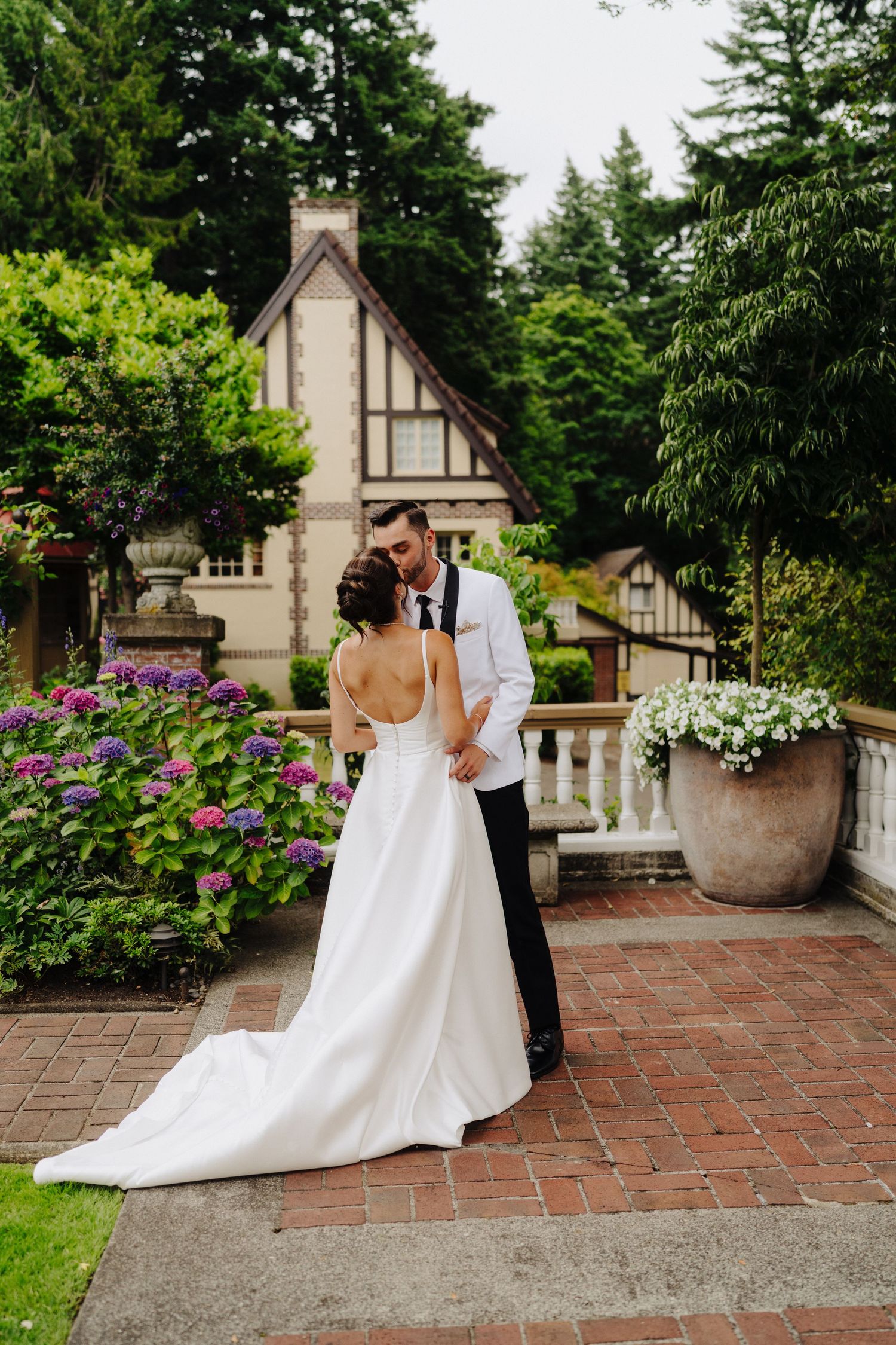 A couple shares an intimate moment on a brick patio surrounded by lush gardens and decorative planters.