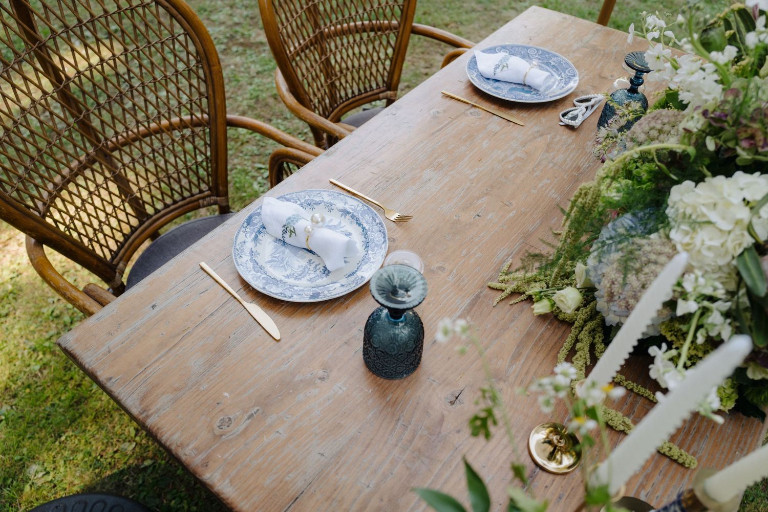 Rustic wooden table set with blue plates and white floral arrangements under outdoor umbrellas.