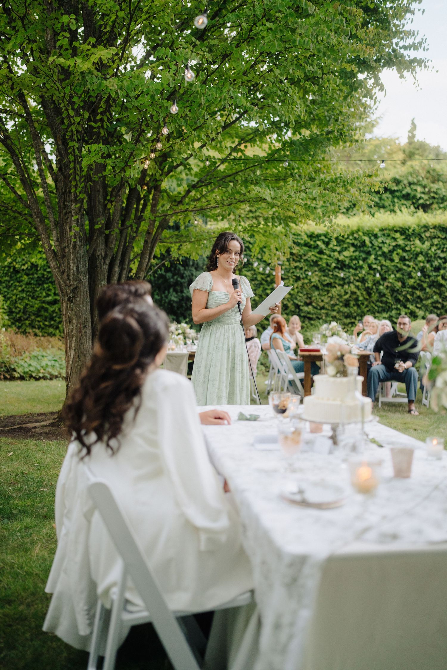 Elegant outdoor wedding reception setup with white tablecloths and natural greenery in a garden setting.