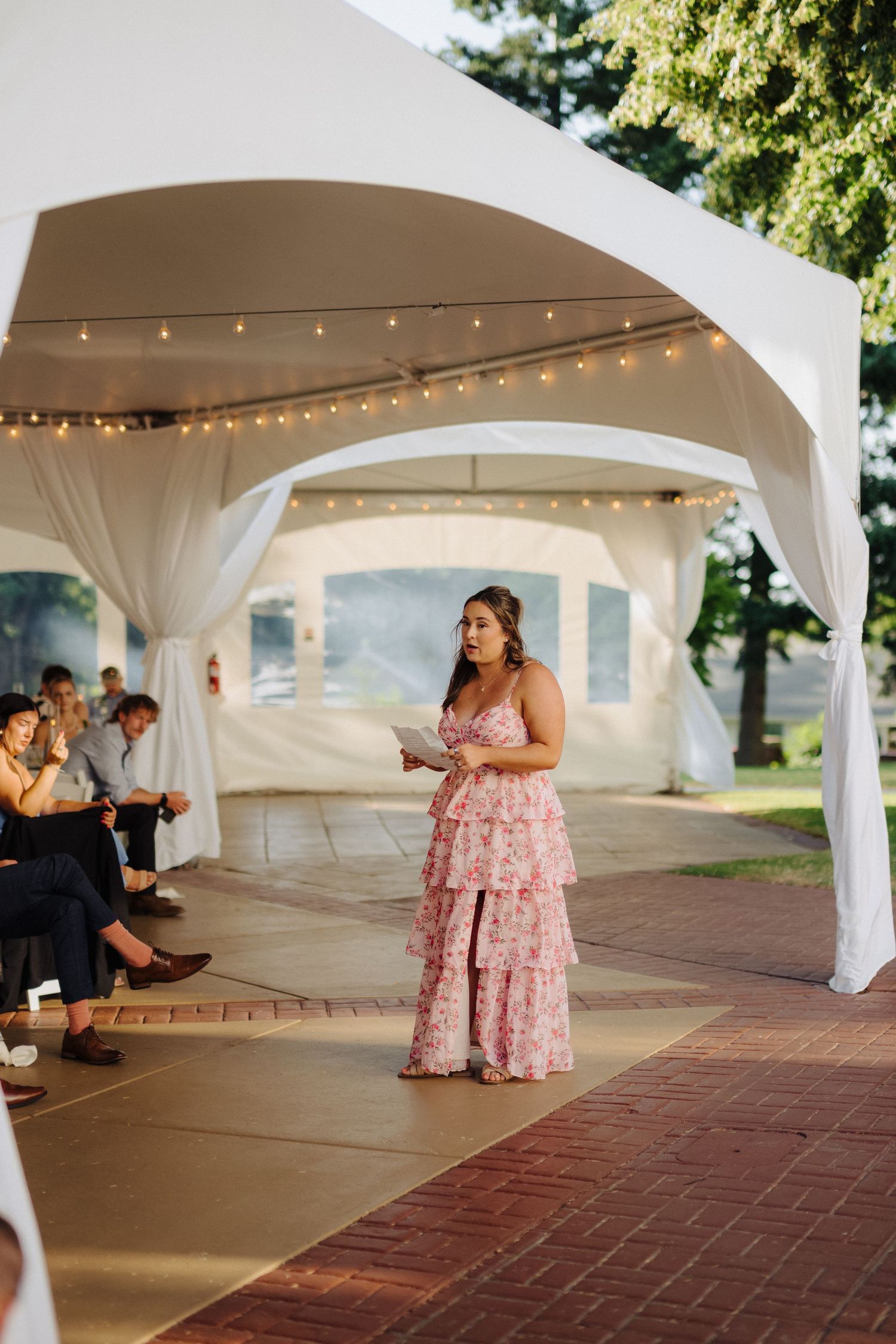 Wedding reception under white tent with string lights and brick patio.
