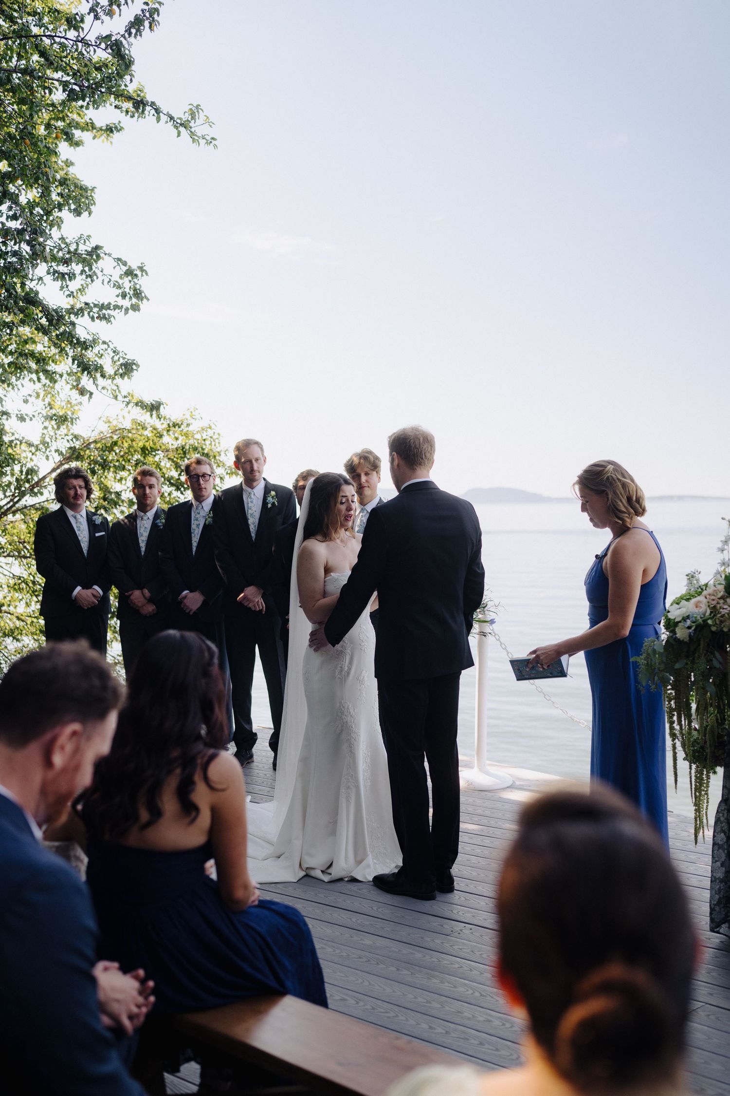 Wedding ceremony in progress on a waterfront deck with guests watching the proceedings.