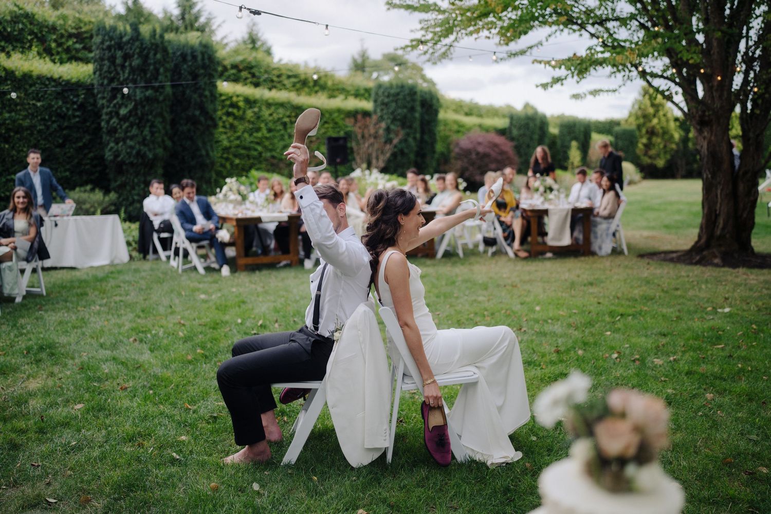 Wedding reception setup in a garden with guests seated at tables under trees.