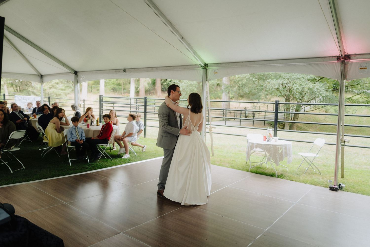 Large white wedding tent set up outdoors with dance floor and guest seating.