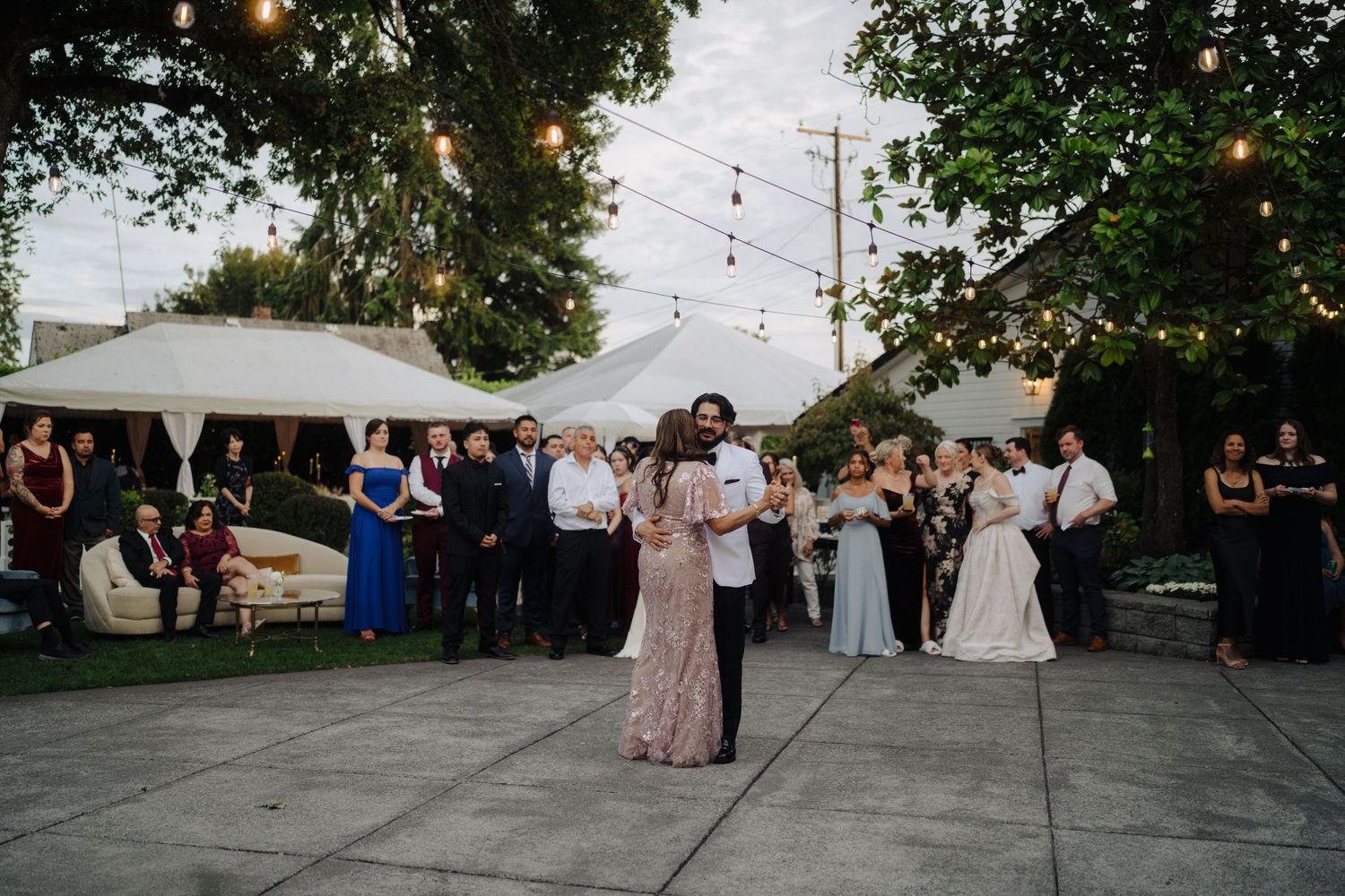 Wedding guests dancing and celebrating on an outdoor patio under string lights at dusk.