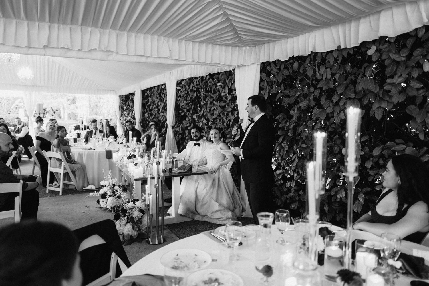 Elegant white tent wedding reception with draped ceiling and formal table settings.