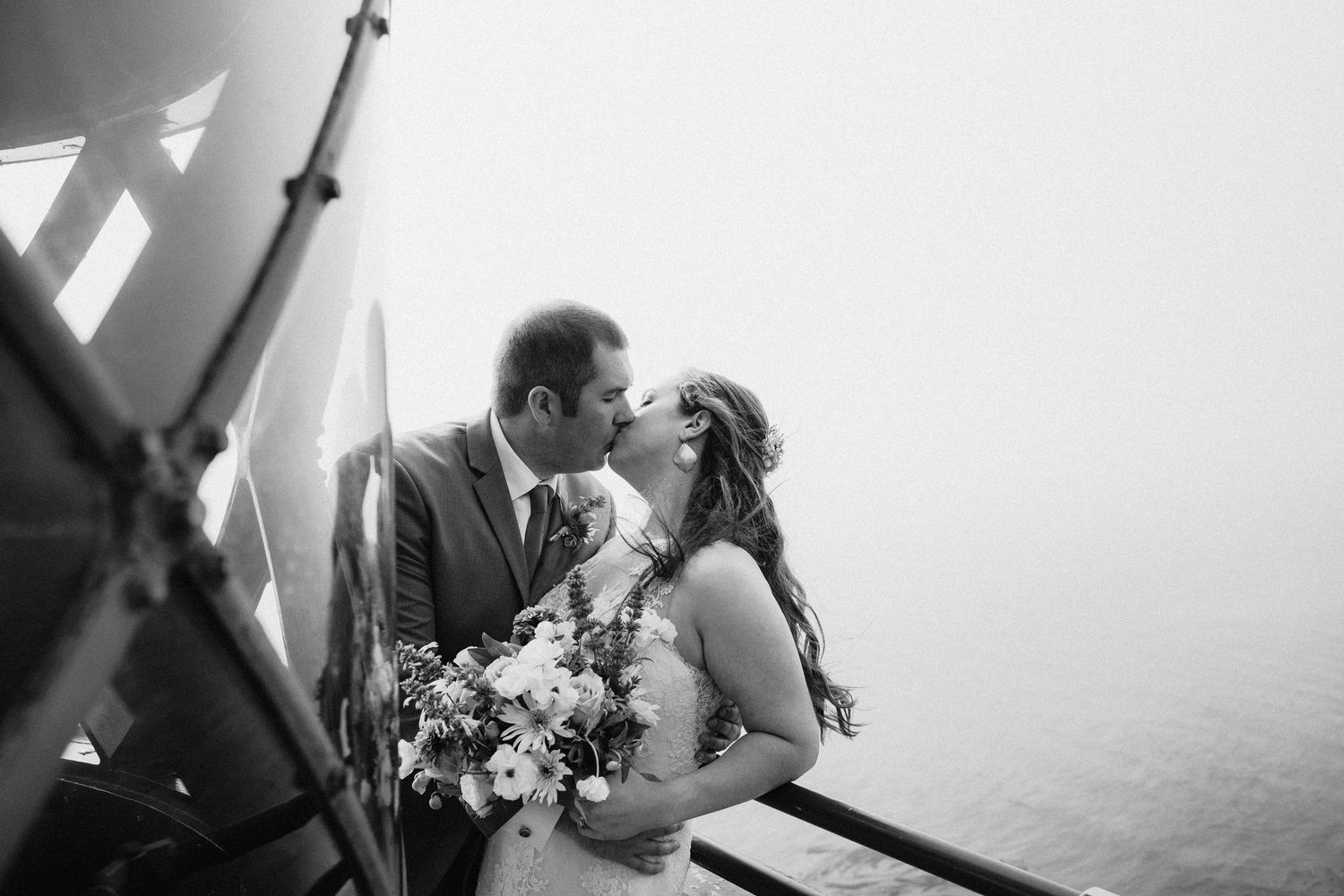 Black and white romantic wedding photo showing couple sharing a tender moment while holding floral bouquet on foggy mountainside.