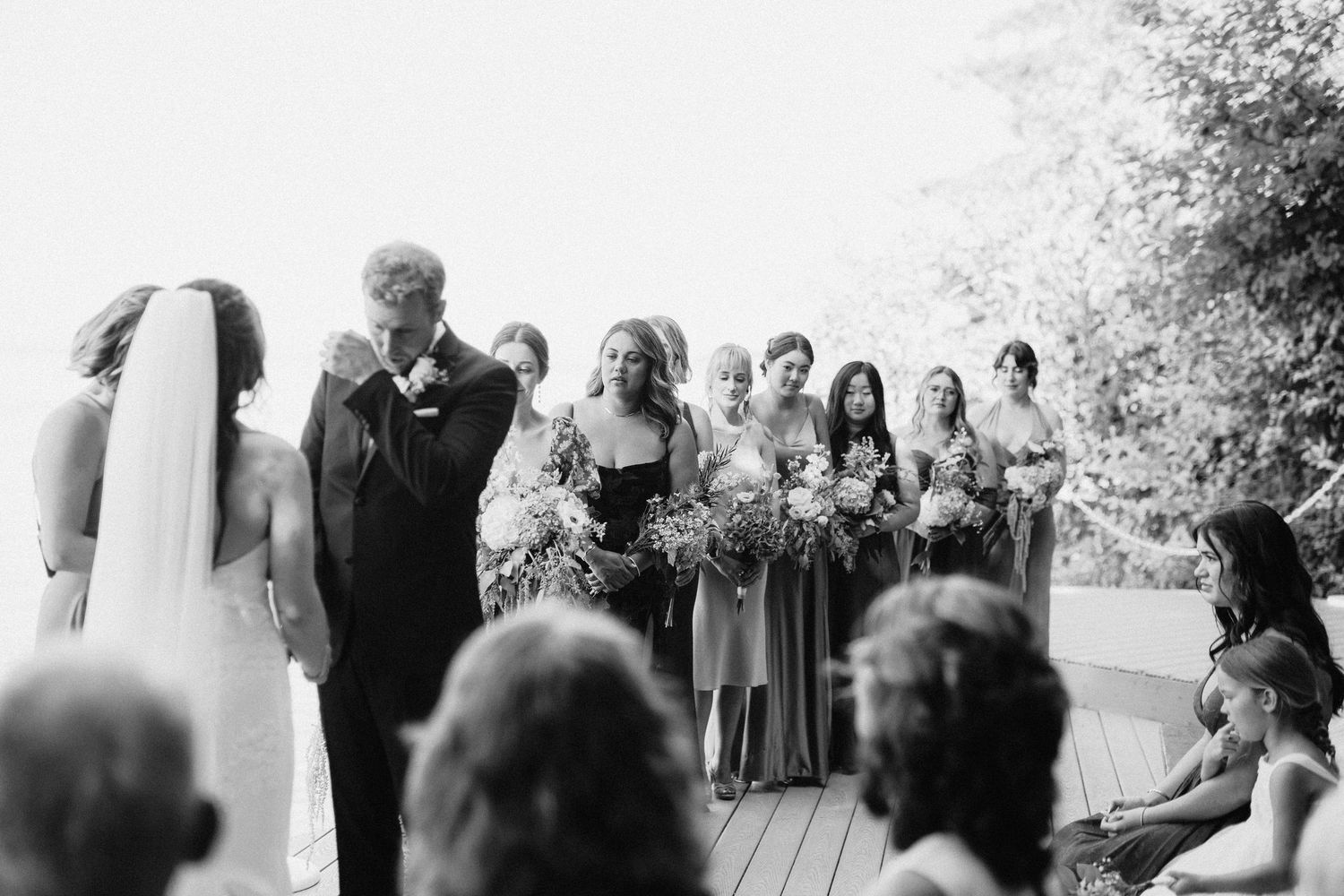 Wedding ceremony gathering on a deck with waterfront views and natural scenery.