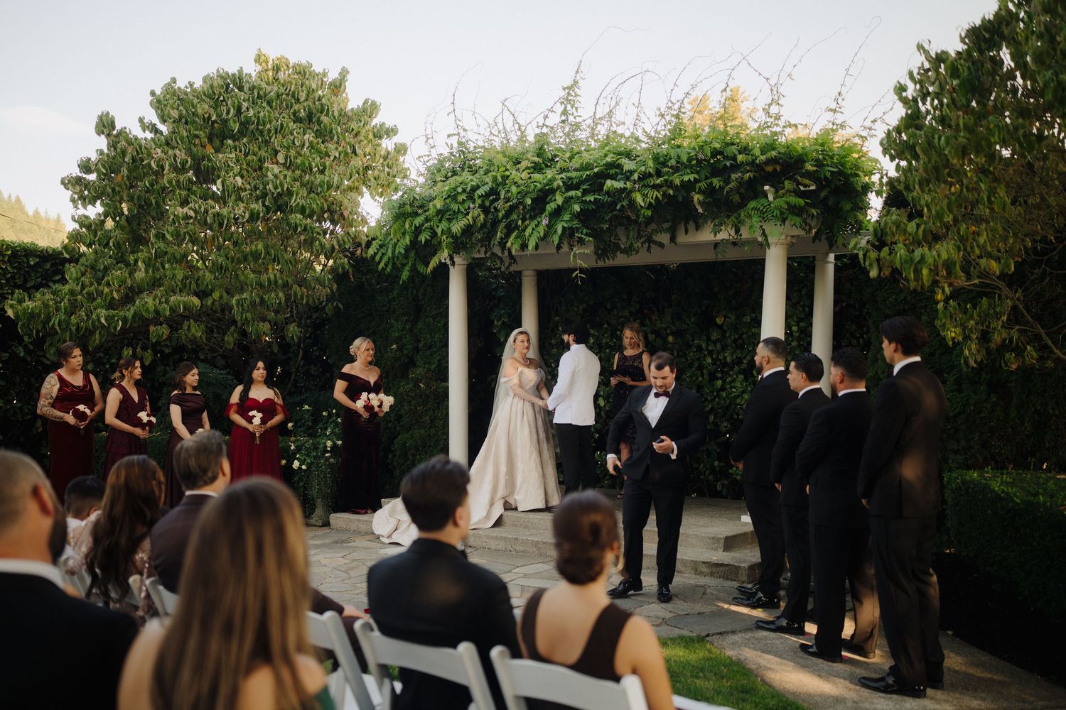 Wedding ceremony setup with white chairs and floral arrangements in an outdoor garden setting.