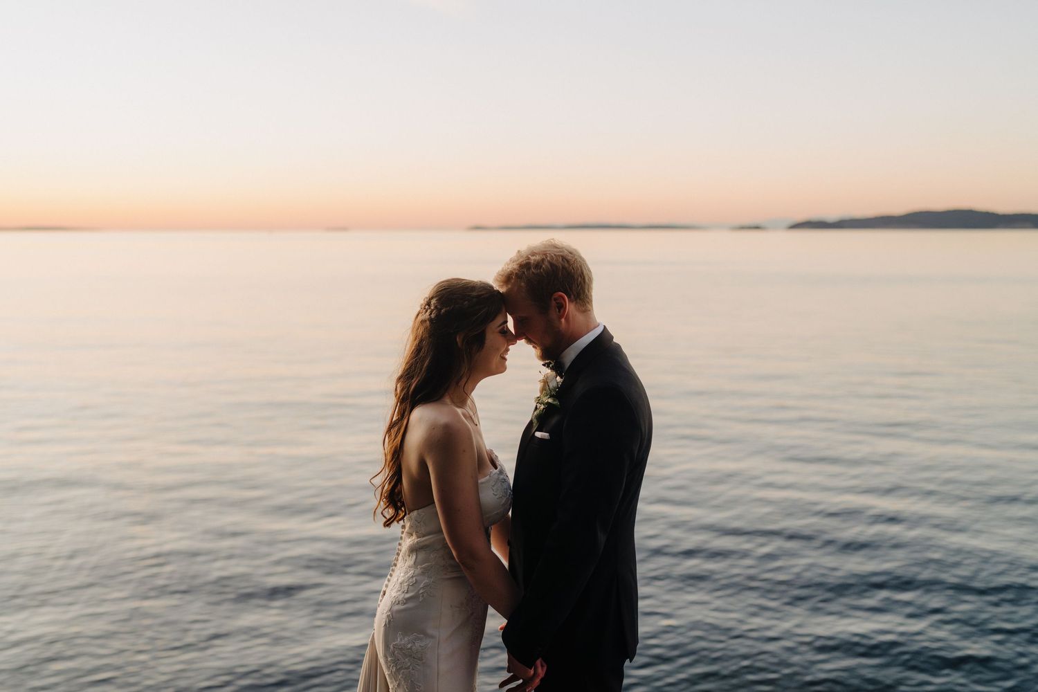 Newlyweds share a romantic moment on a wooden pier overlooking a serene lake at dusk.