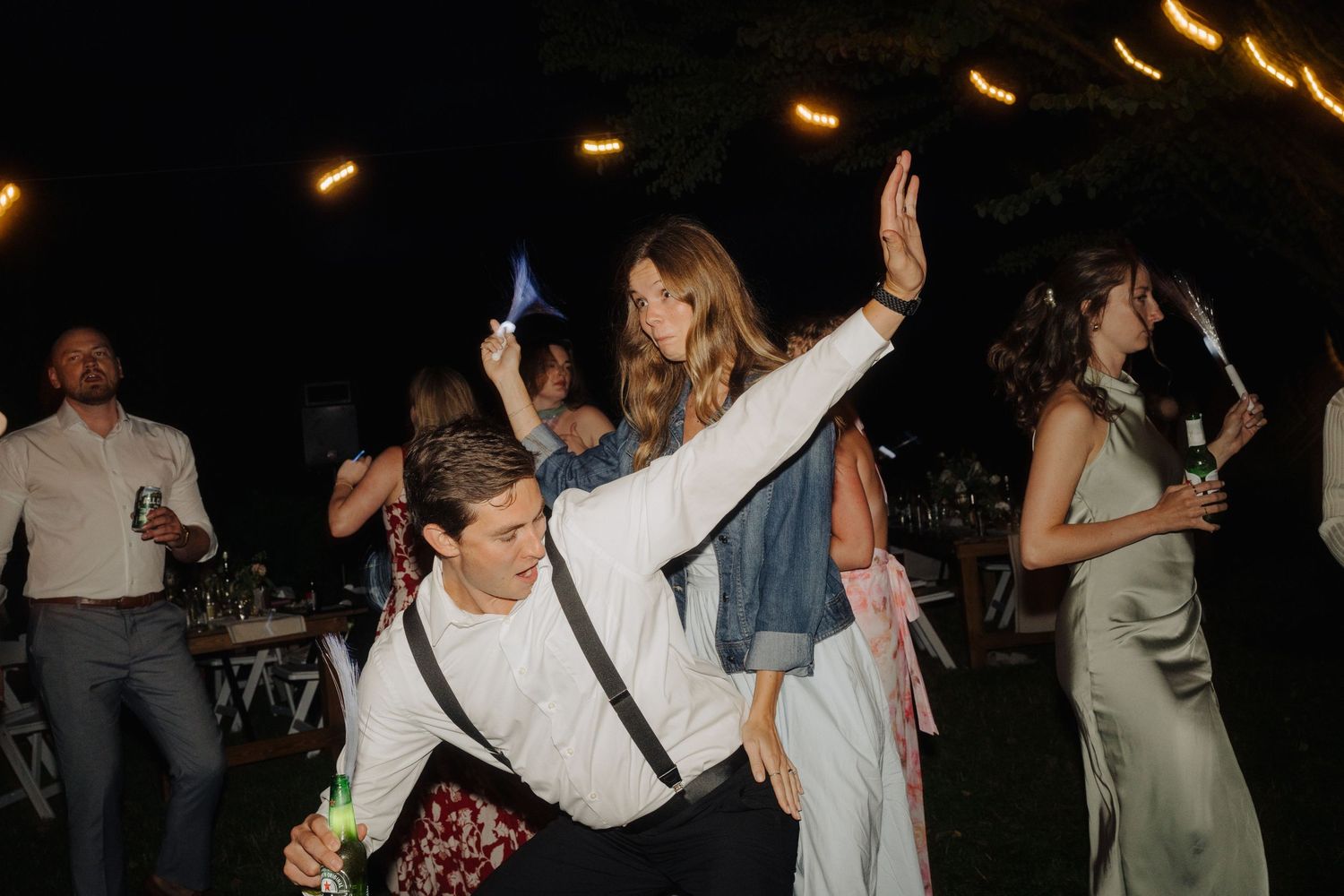 Partygoers dance beneath string lights at a nighttime outdoor celebration.