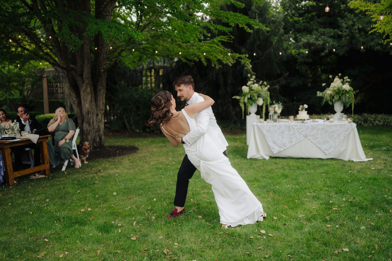 Guests celebrate at an outdoor garden wedding with white decorations and natural greenery.