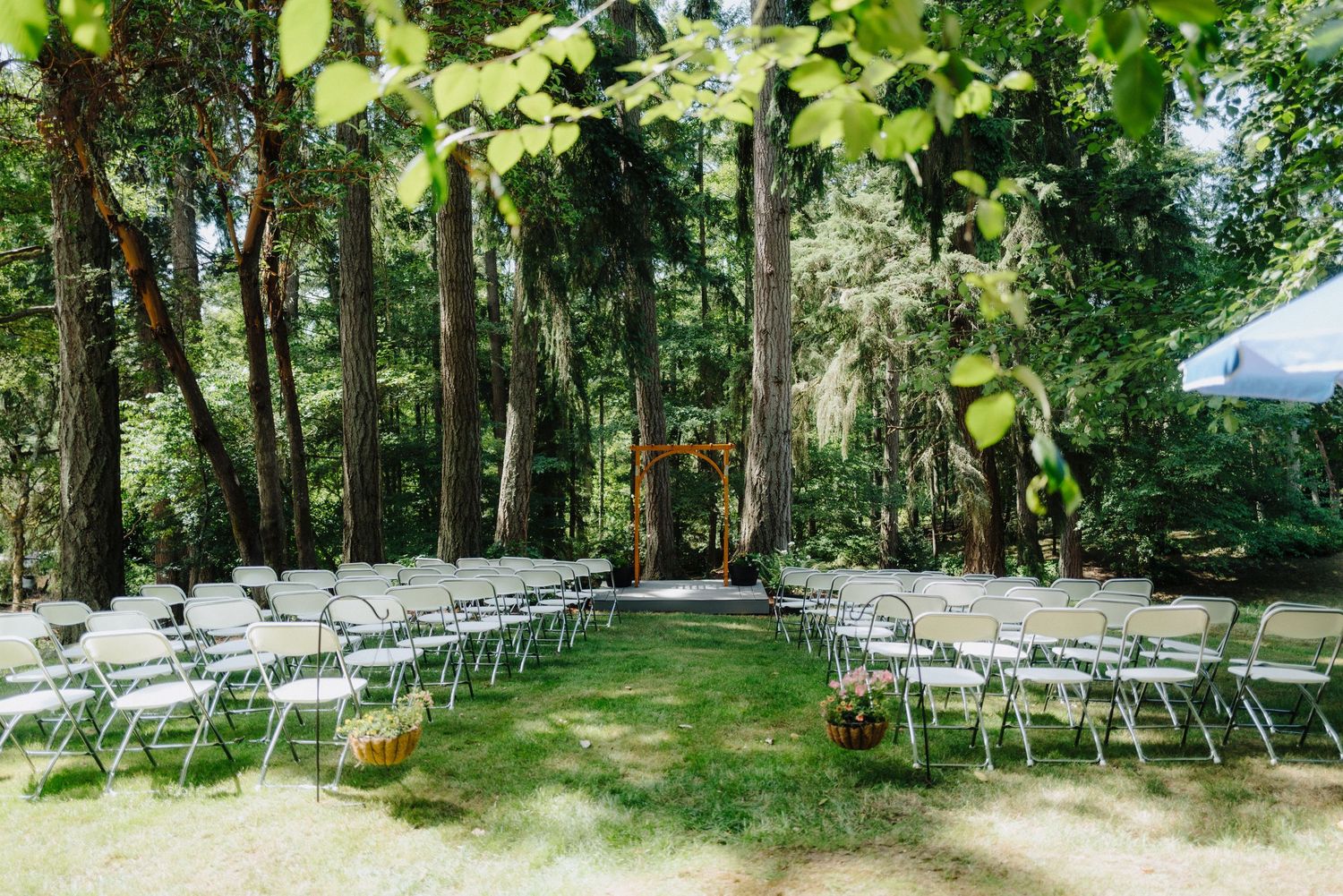 White folding chairs set up for outdoor wedding ceremony in wooded forest setting.