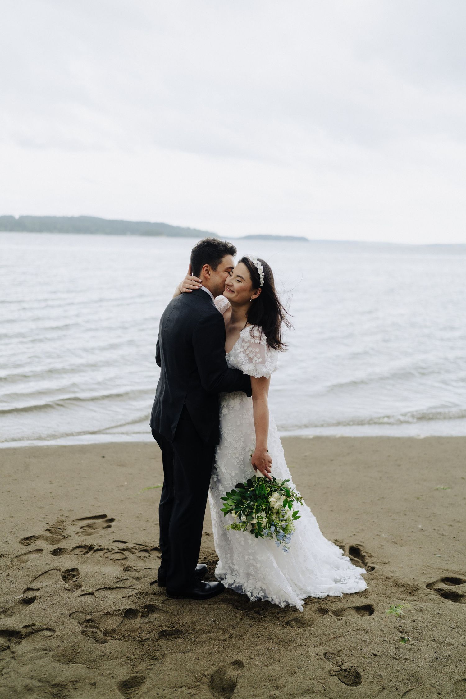 A romantic moment between newlyweds on a cloudy beach with waves in the background.