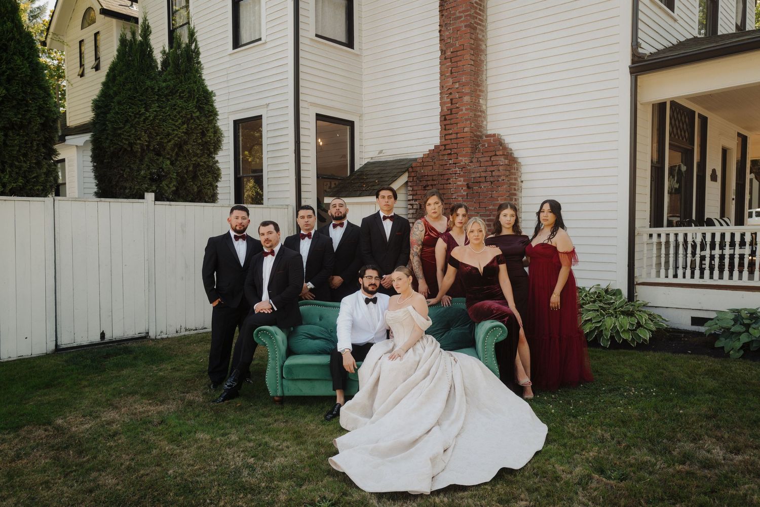 Wedding party posing on a teal vintage couch in front of a white historic house.