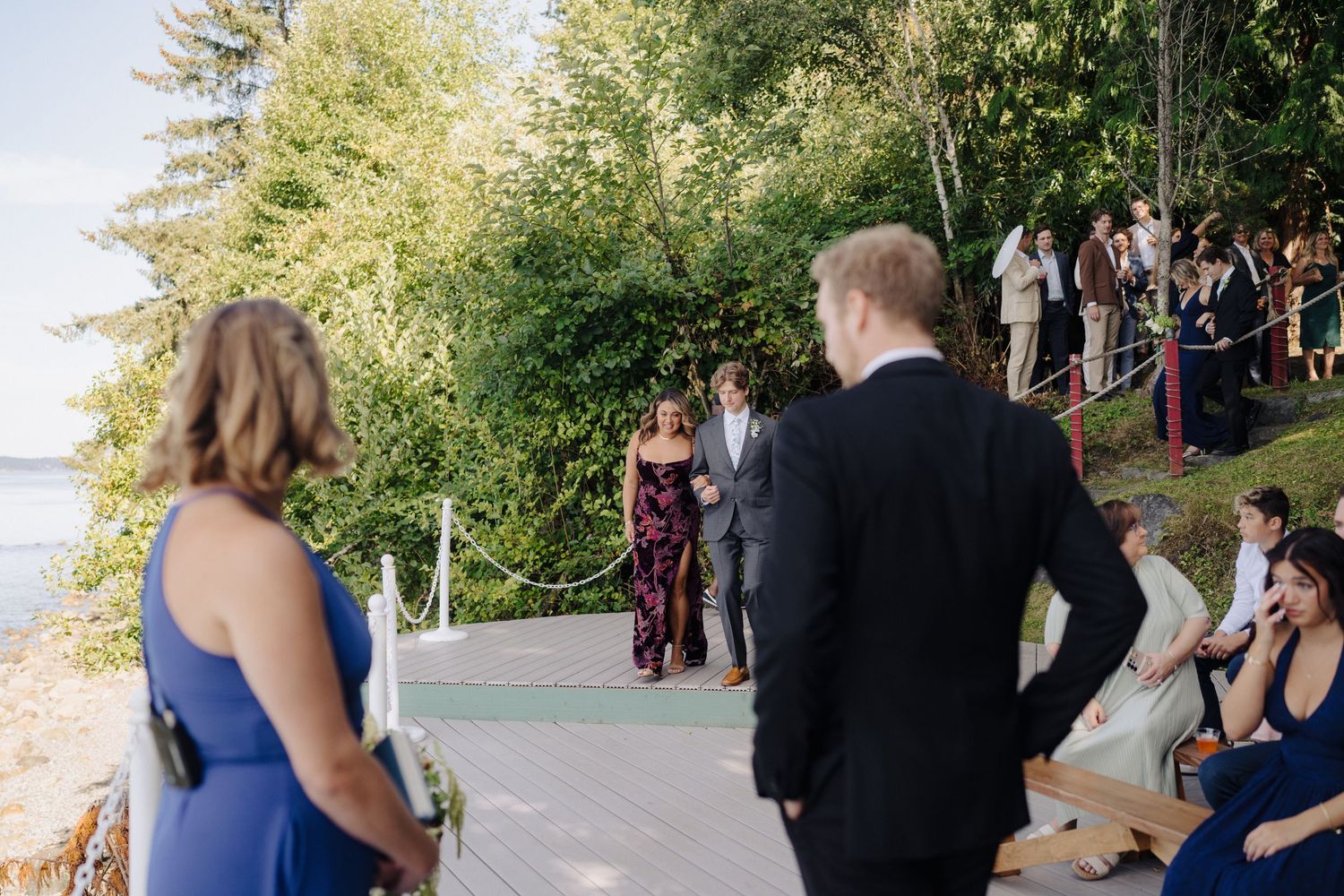 Outdoor wedding ceremony setup on a waterfront deck with guests seated in formal attire.