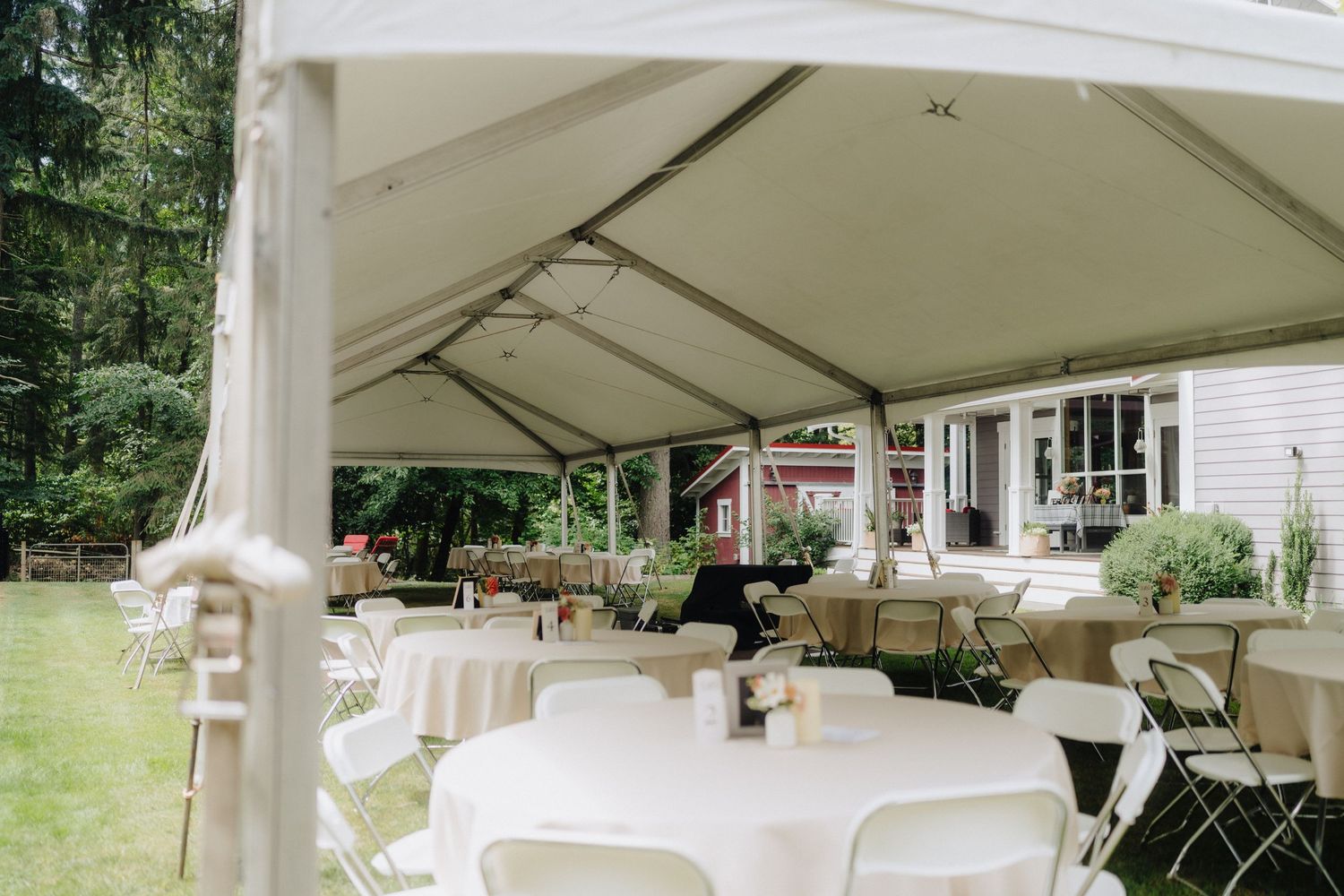 White tent setup for outdoor wedding reception with tables and chairs arranged underneath.
