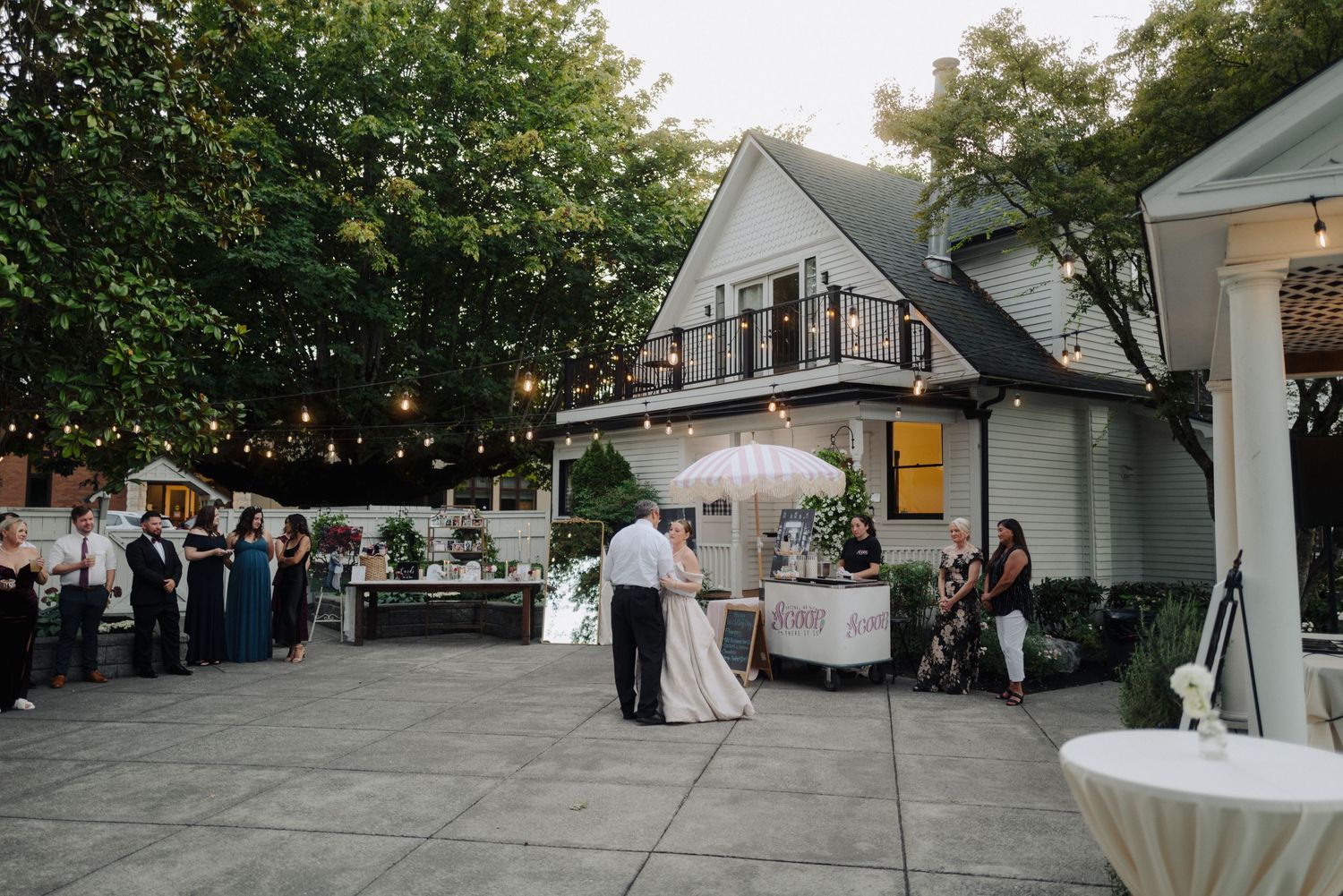 Wedding reception venue setup with string lights and white tents in garden setting.