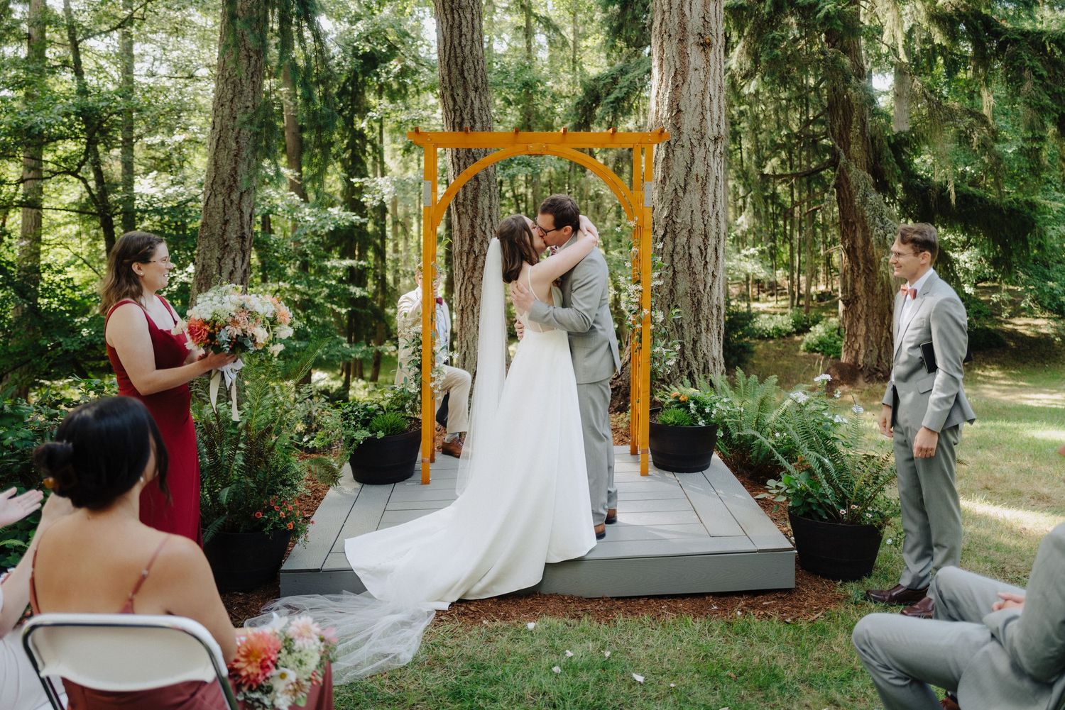 Outdoor wedding ceremony setup with wooden arch and chairs in a forest setting.
