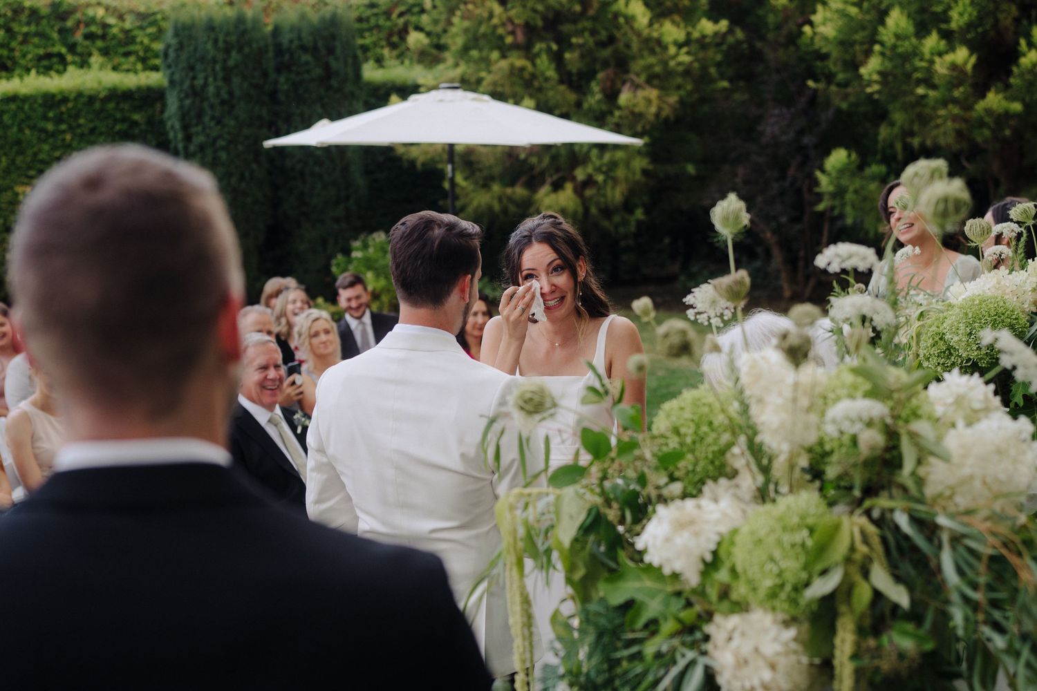 Garden wedding ceremony with white umbrellas and lush floral arrangements.