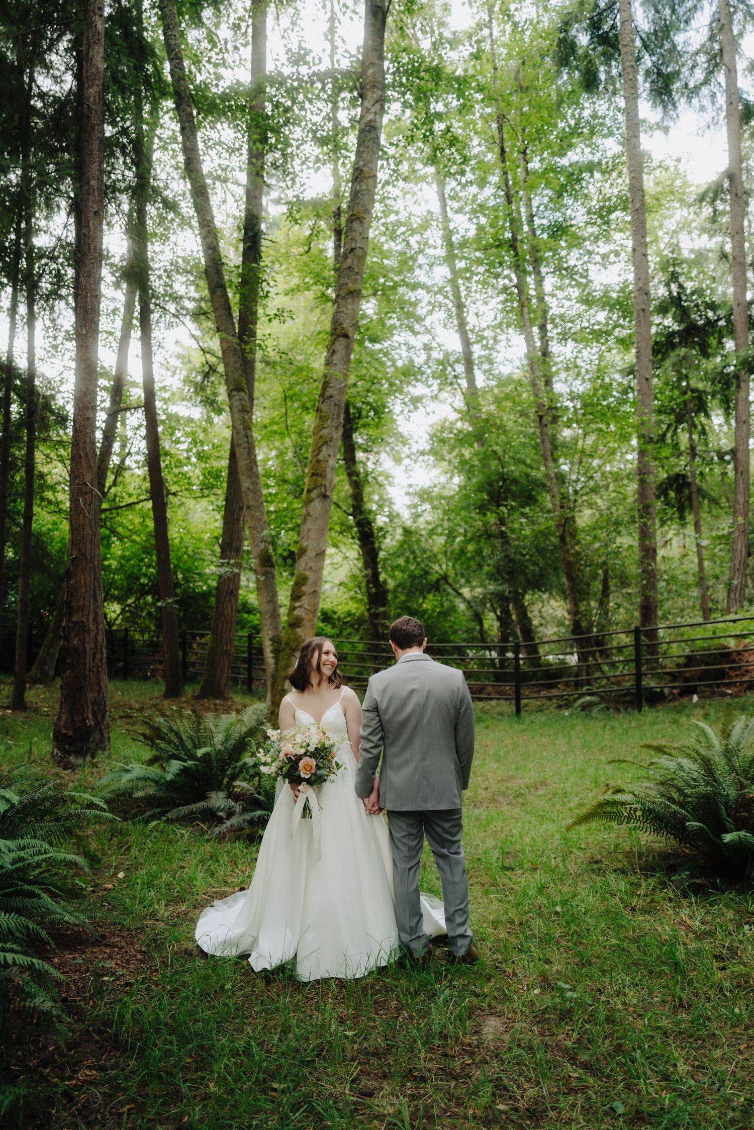 A romantic wedding moment captured in a lush green forest setting with ferns and tall trees.