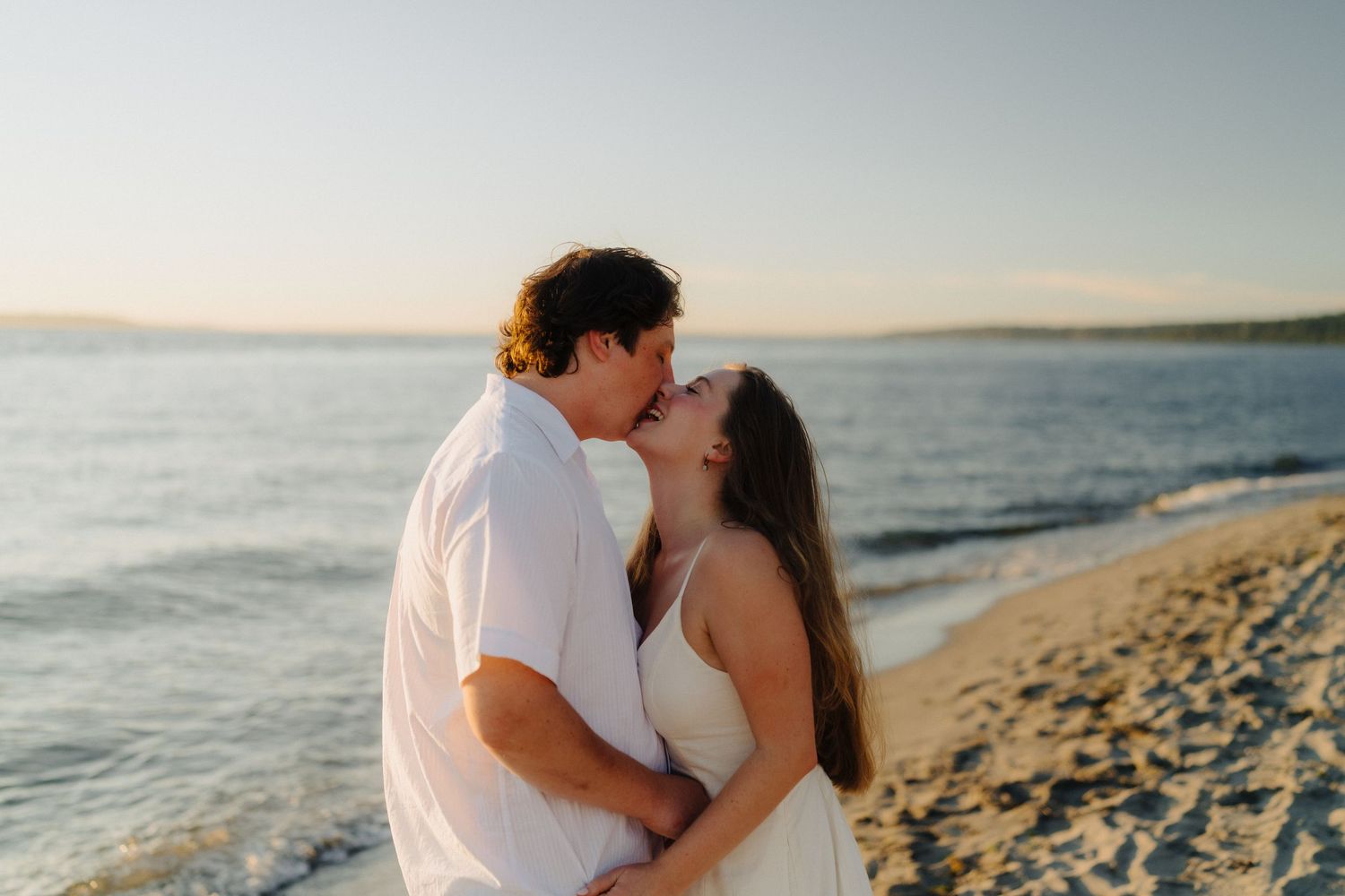 A romantic couple shares a tender moment on a scenic beach at sunset with the ocean waves in the background.