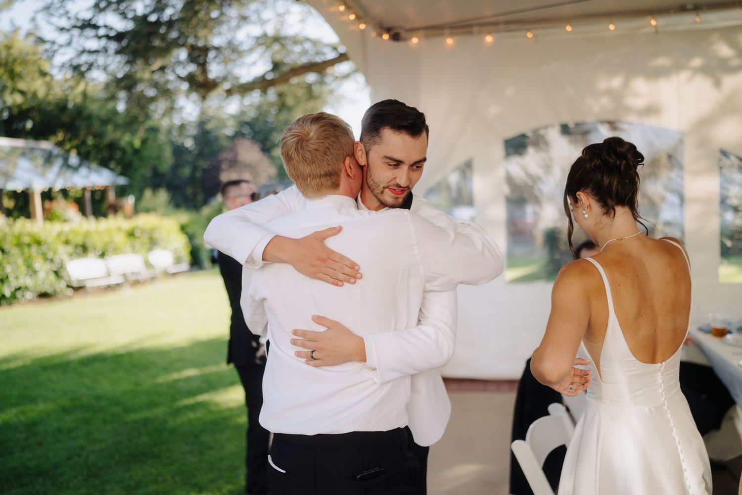 Wedding couple and guests dancing outdoors under string lights at sunset reception.
