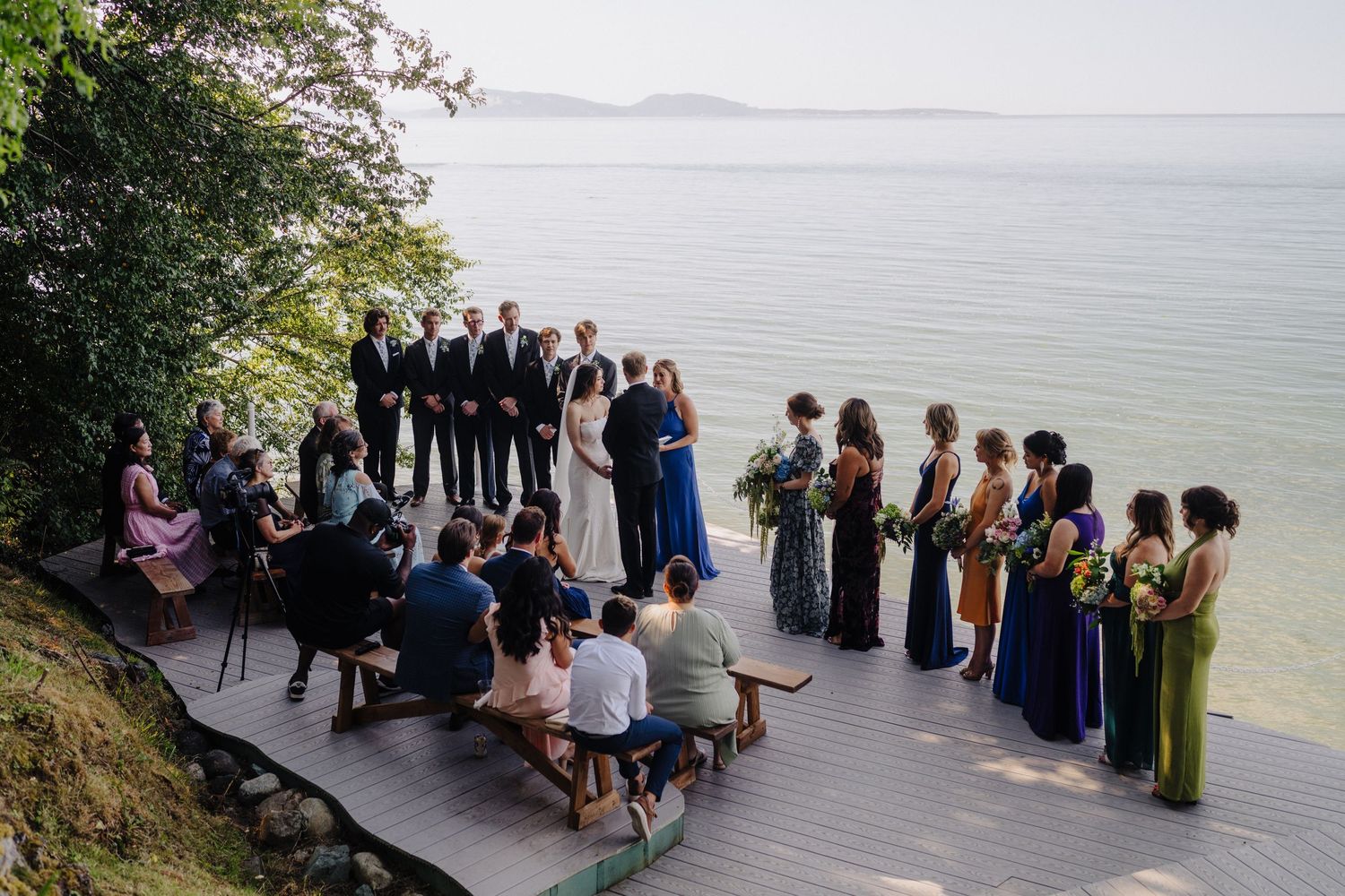 Wedding guests seated in rows on a deck overlooking a serene waterfront landscape.