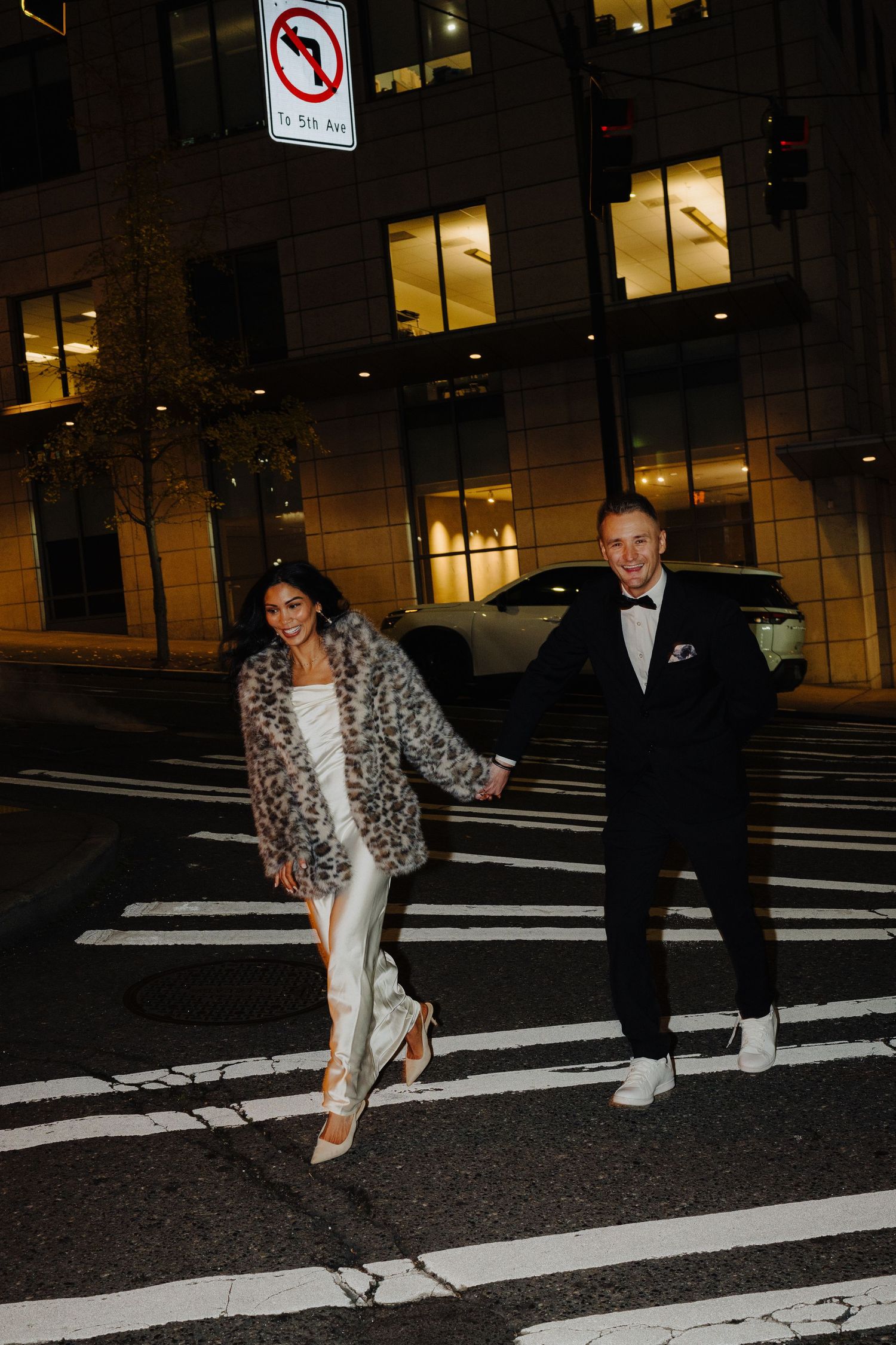 A couple crosses a city street at night, with the bride wearing a leopard print coat over her gown.