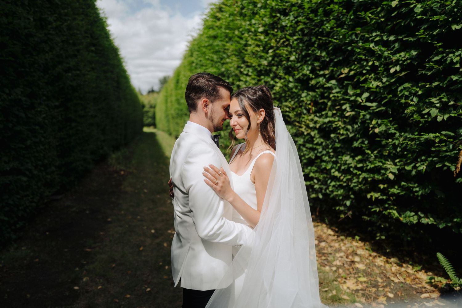 Romantic wedding portrait in a formal garden with manicured hedge walls creating a natural corridor.