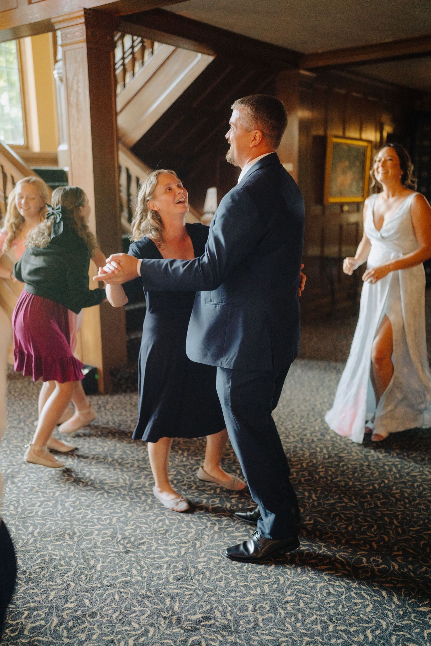 Wedding guests dancing and celebrating on a patterned carpet at an indoor reception.